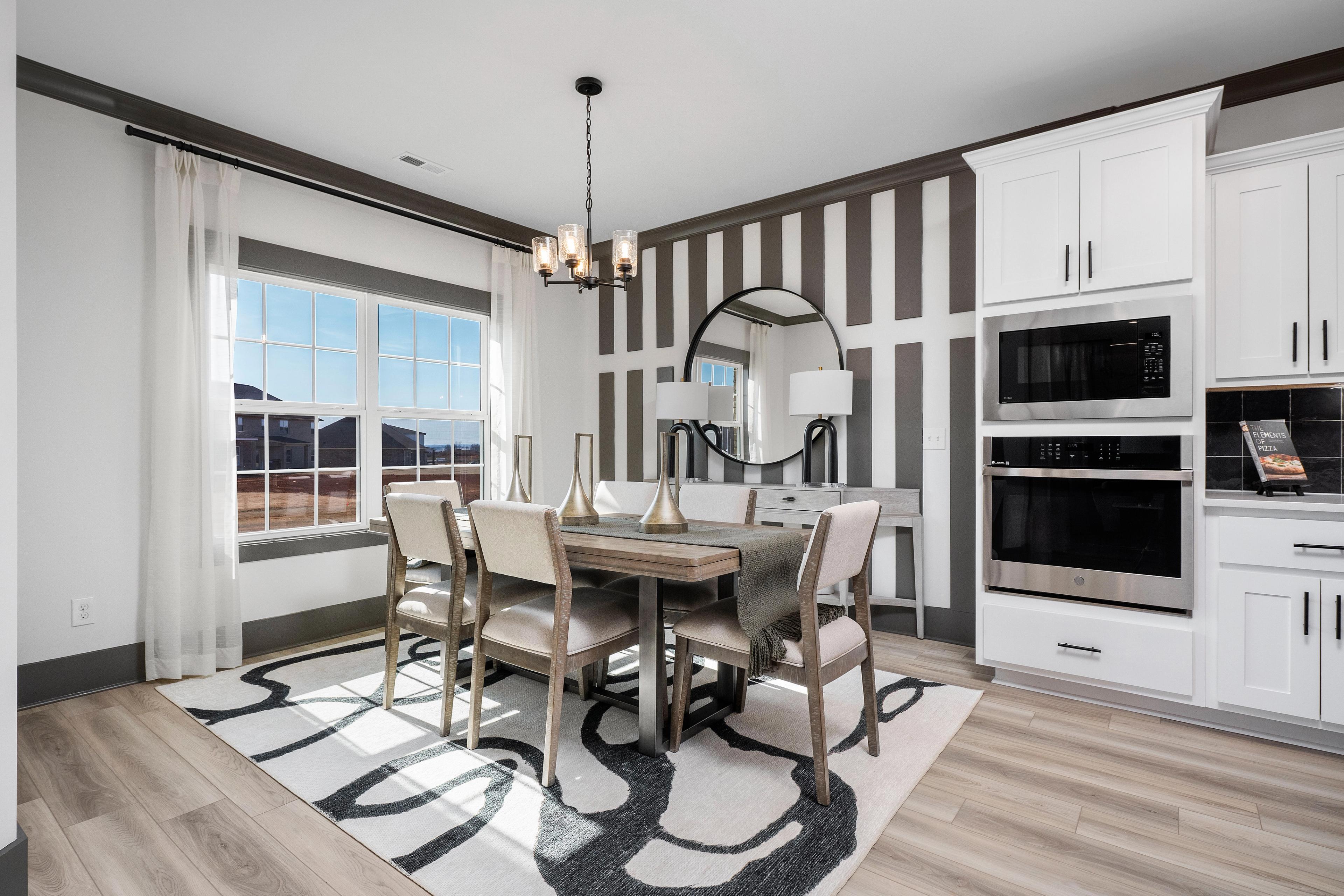 Elegant dining room at Barnett's Crossing in Madison, AL with wooden table, chandelier, striped accent wall, and open white kitchen