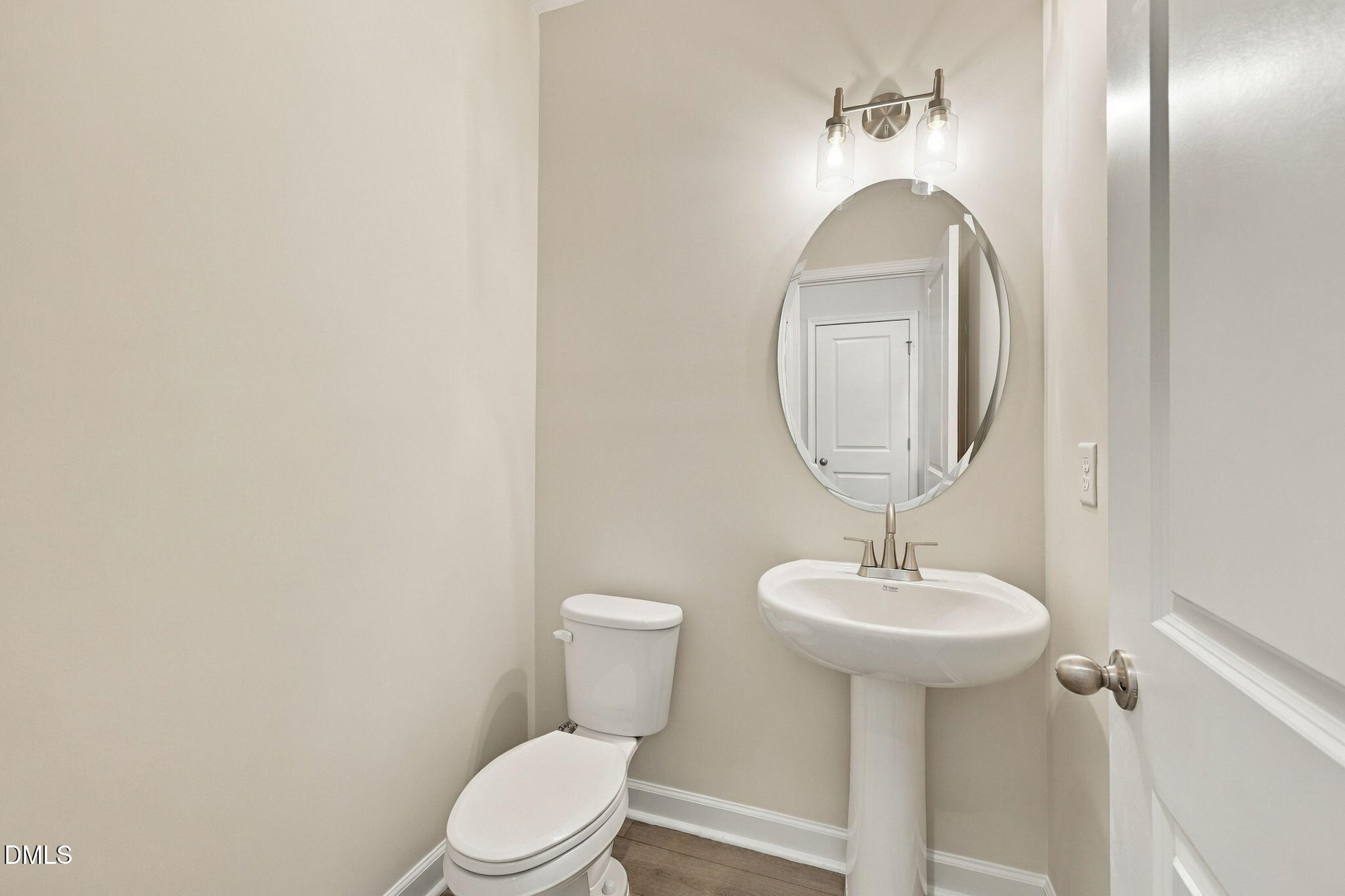 Elegant half bath with pedestal sink, oval mirror, and brushed nickel fixtures in Davidson Homes The Alexander B, Knightdale, NC