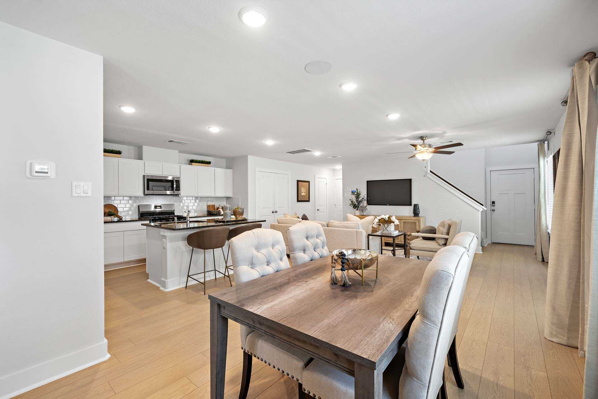 Open-concept kitchen and dining area at Haven at Kieth Harrow in Cypress Texas with white cabinets, island, and hardwood floors