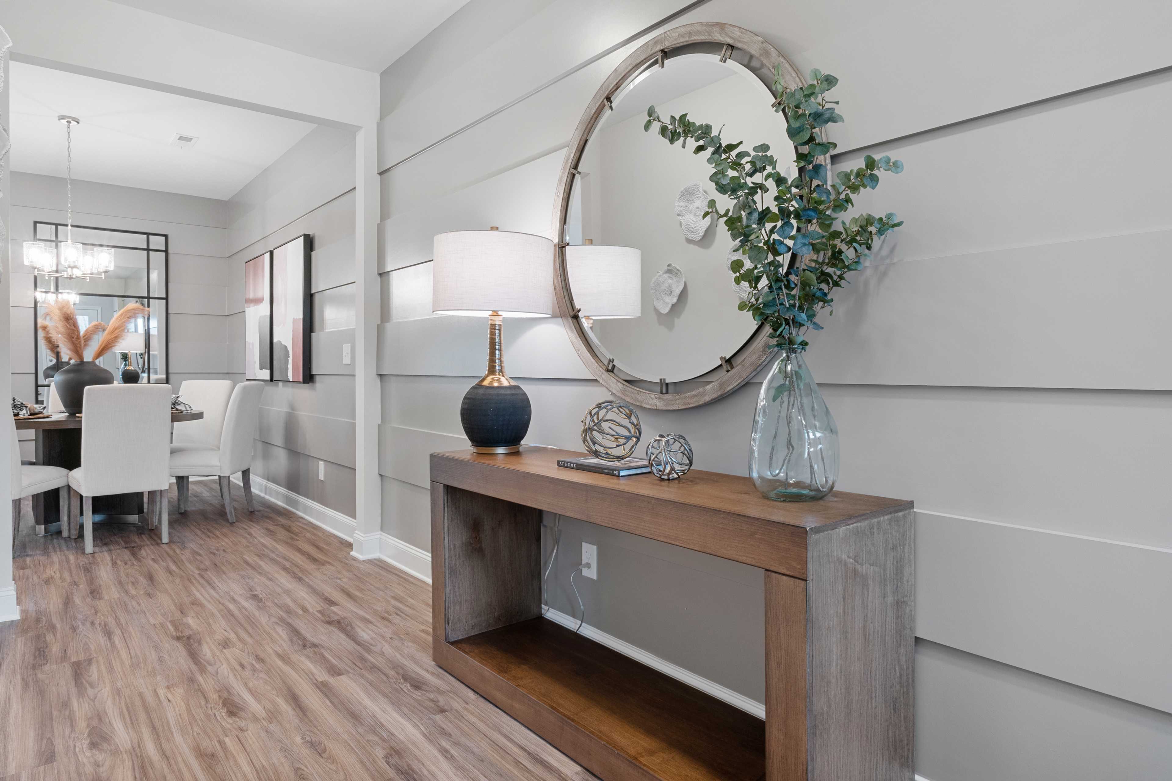 Spacious entryway at The Retreat at Cain Park in Hartselle Alabama featuring wooden console table, round mirror, lamp, eucalyptus, and hardwood floors
