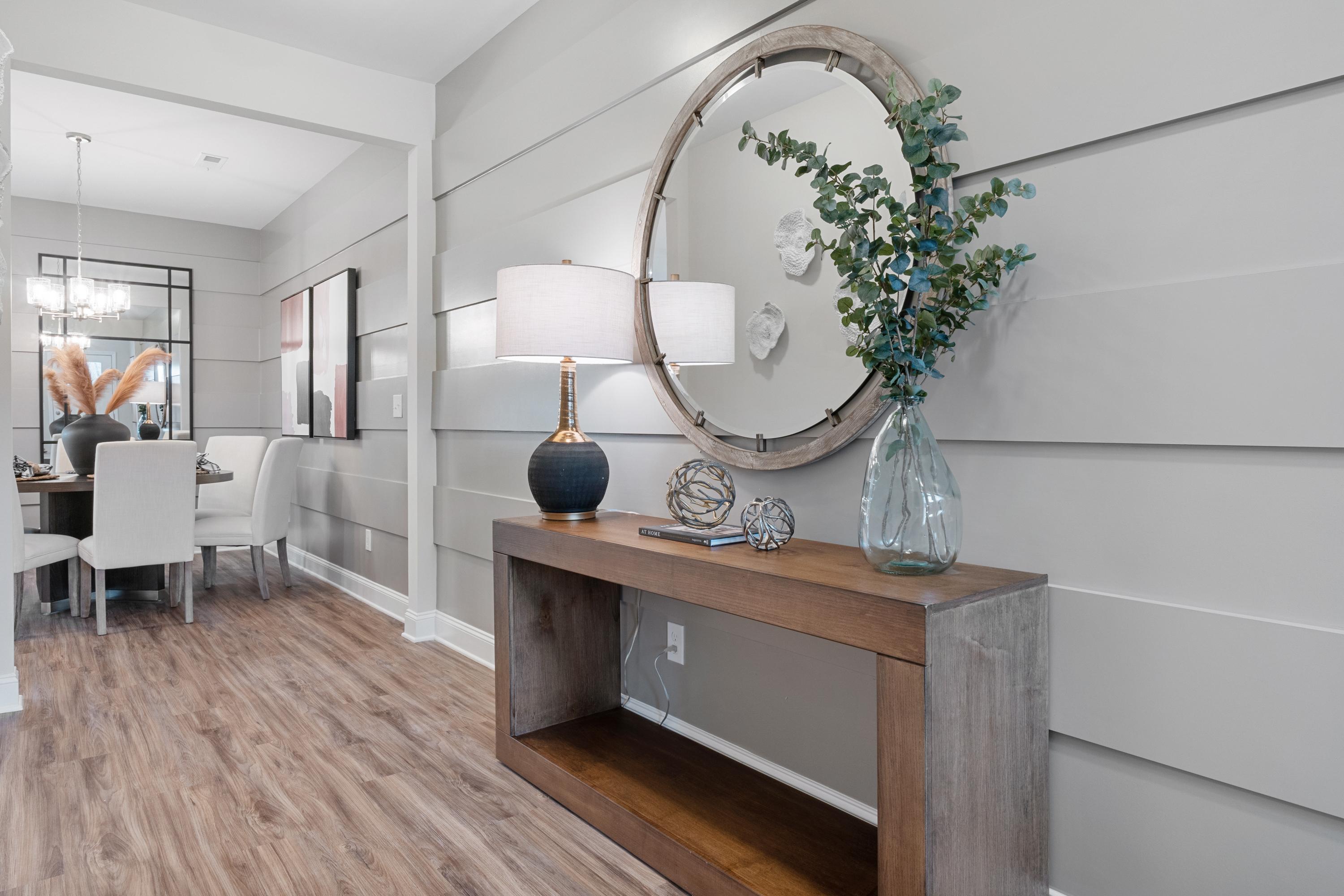 Spacious entryway at The Retreat at Cain Park in Hartselle Alabama featuring wooden console table, round mirror, lamp, eucalyptus, and hardwood floors