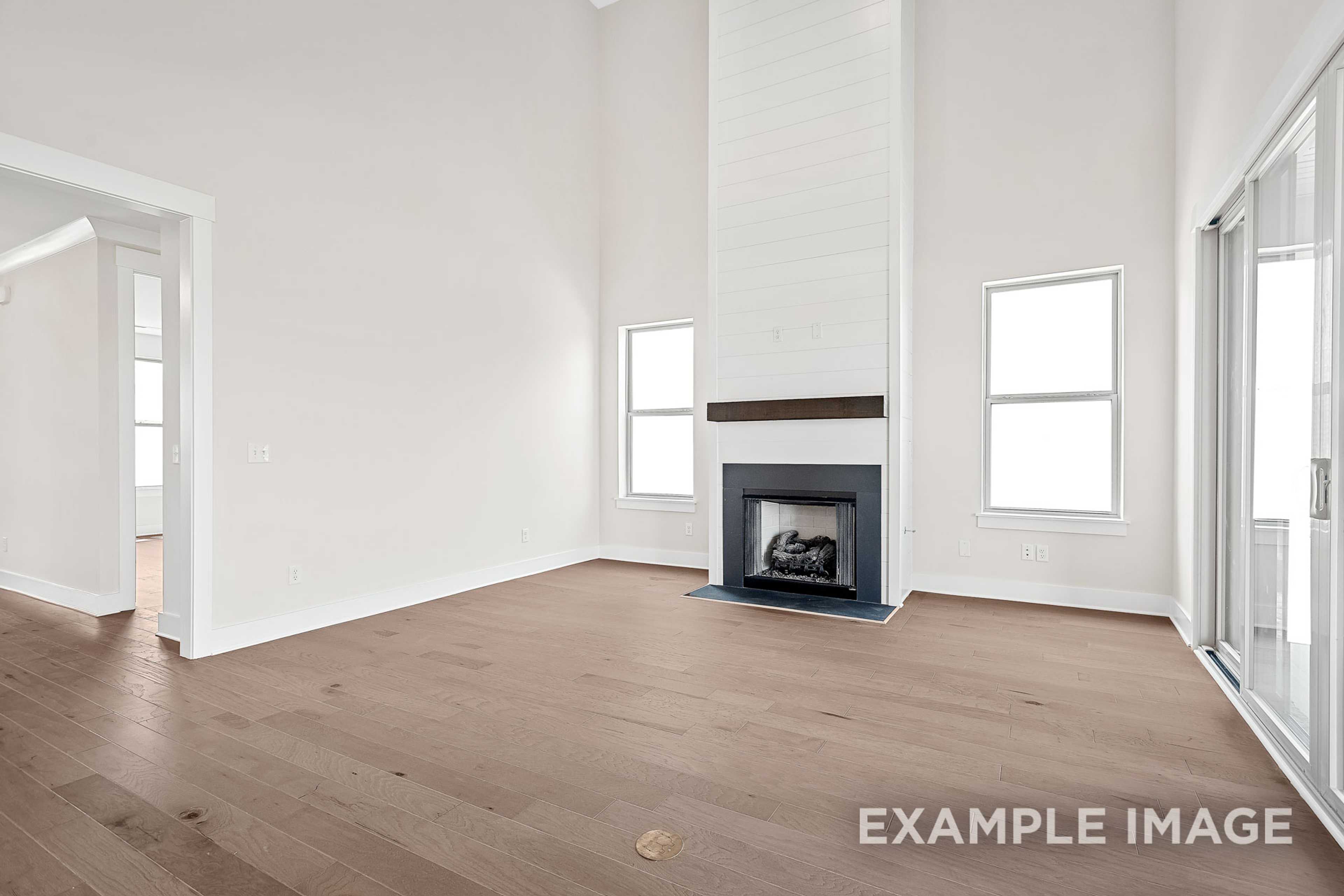 Spacious living room in The Hawkins with white shiplap fireplace, hardwood floors, large windows, and sliding glass doors