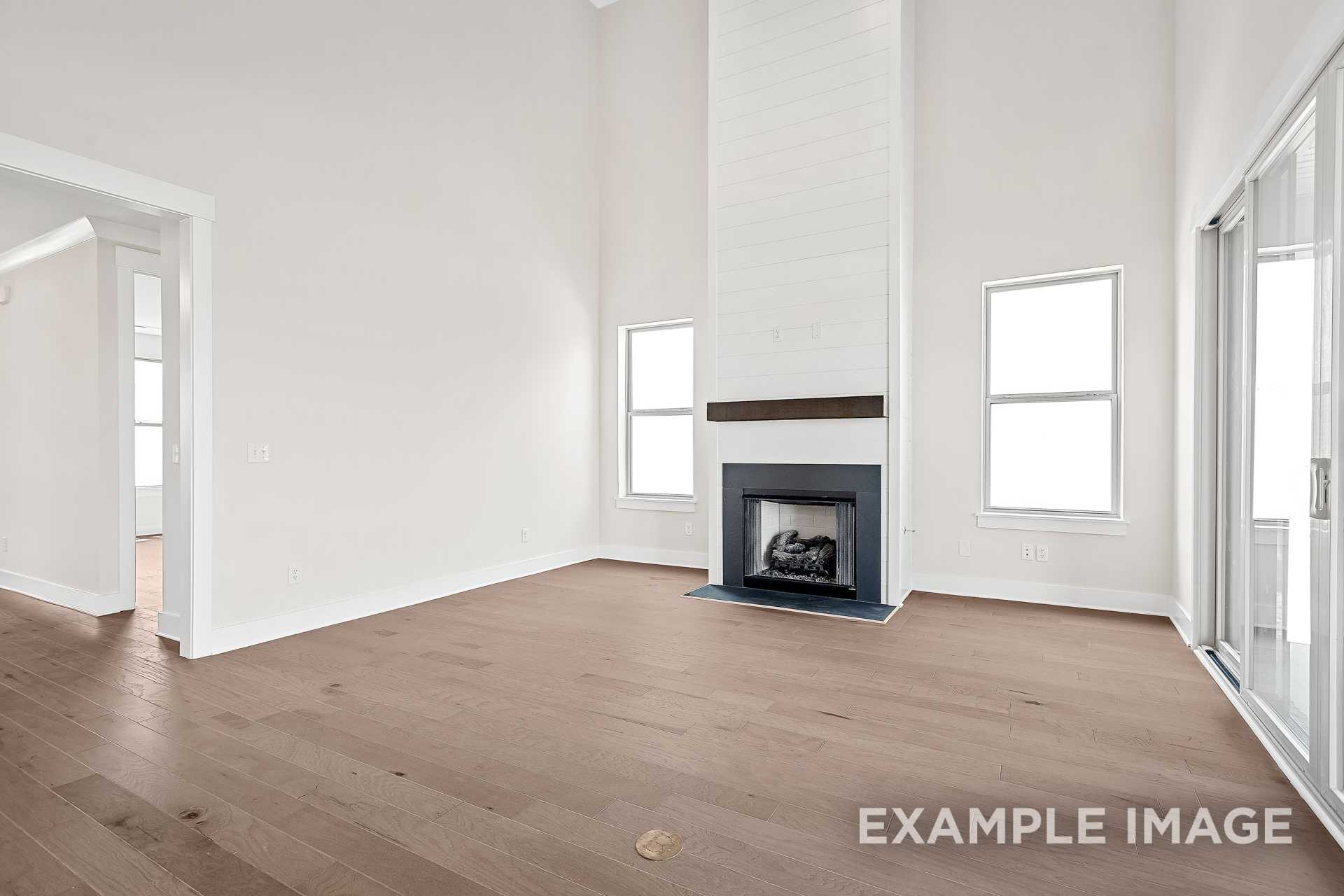 Spacious living room in The Hawkins with white shiplap fireplace, hardwood floors, large windows, and sliding glass doors