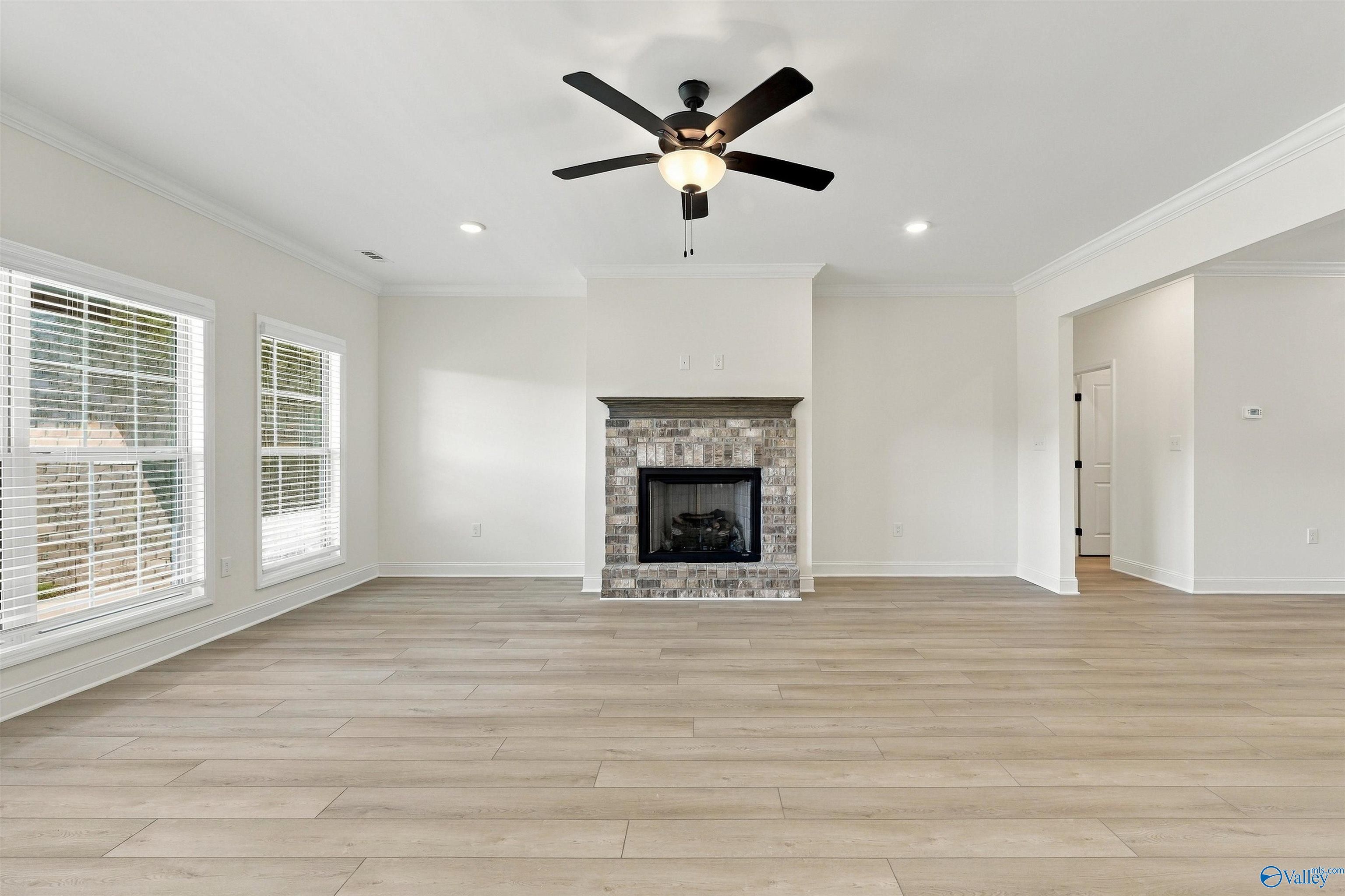 Bright great room with brick fireplace, ceiling fan, and luxury vinyl plank flooring in The Valencia at Riverton Preserve, Huntsville