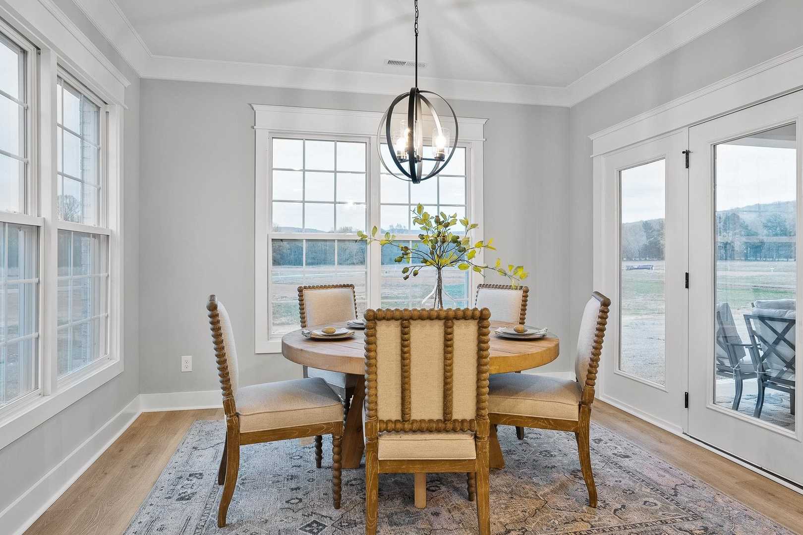 Spacious dining room in The Oxford home with round wood table, upholstered chairs, chandelier, large windows, and French doors to patio