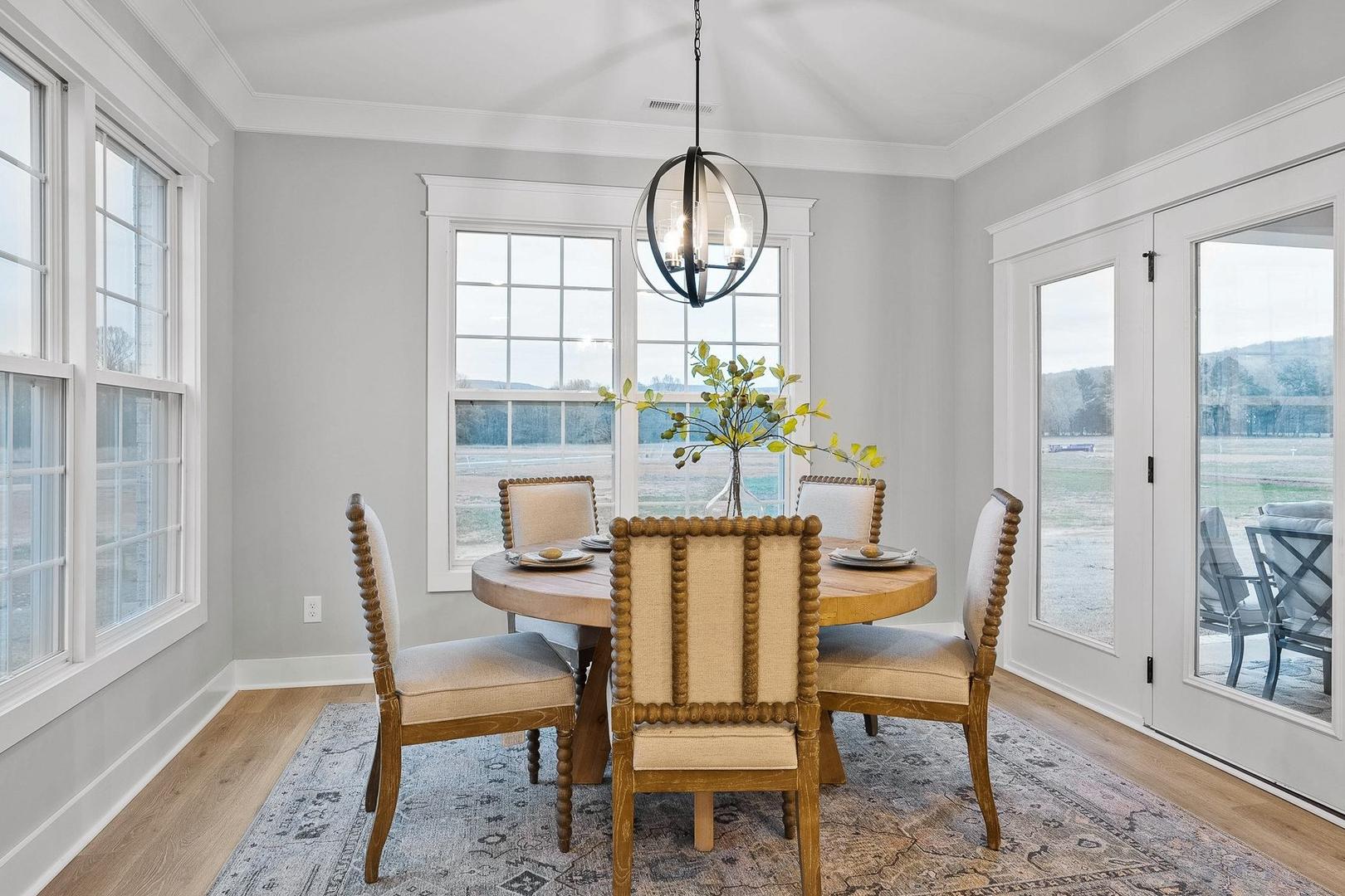 Spacious dining room in The Oxford home with round wood table, upholstered chairs, chandelier, large windows, and French doors to patio