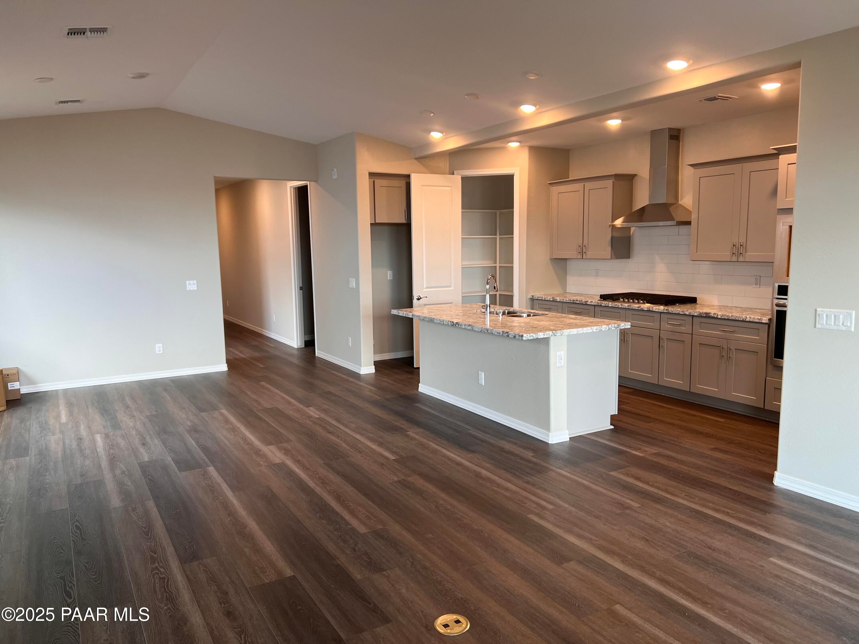 Modern open kitchen with white shaker cabinets, quartz island sink, stainless steel appliances, and luxury vinyl plank flooring in Davidson Homes The Frontier A, Prescott Valley