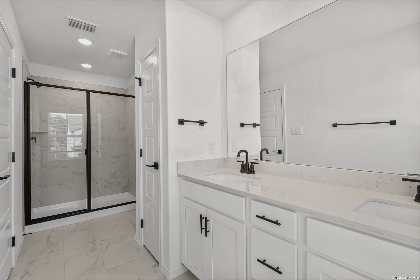 Modern bathroom with dual vanity, quartz countertops, and walk-in tiled shower in The Gillian C home, San Antonio, Texas.