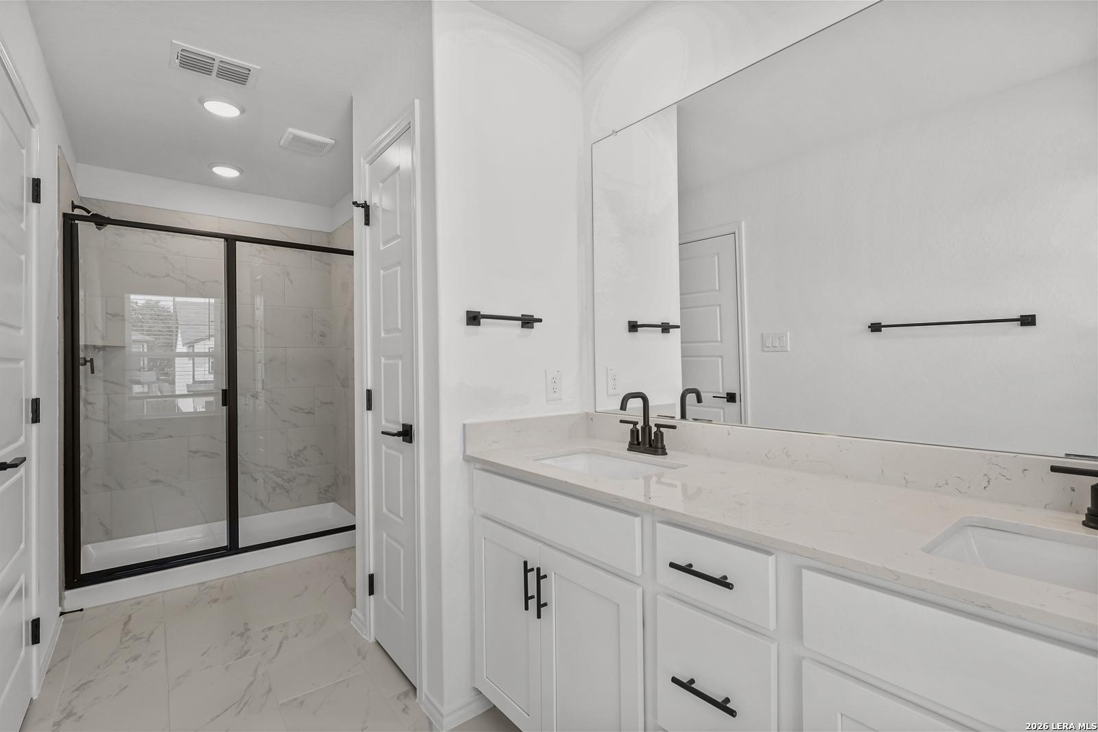 Modern bathroom with dual vanity, quartz countertops, and walk-in tiled shower in The Gillian C home, San Antonio, Texas.