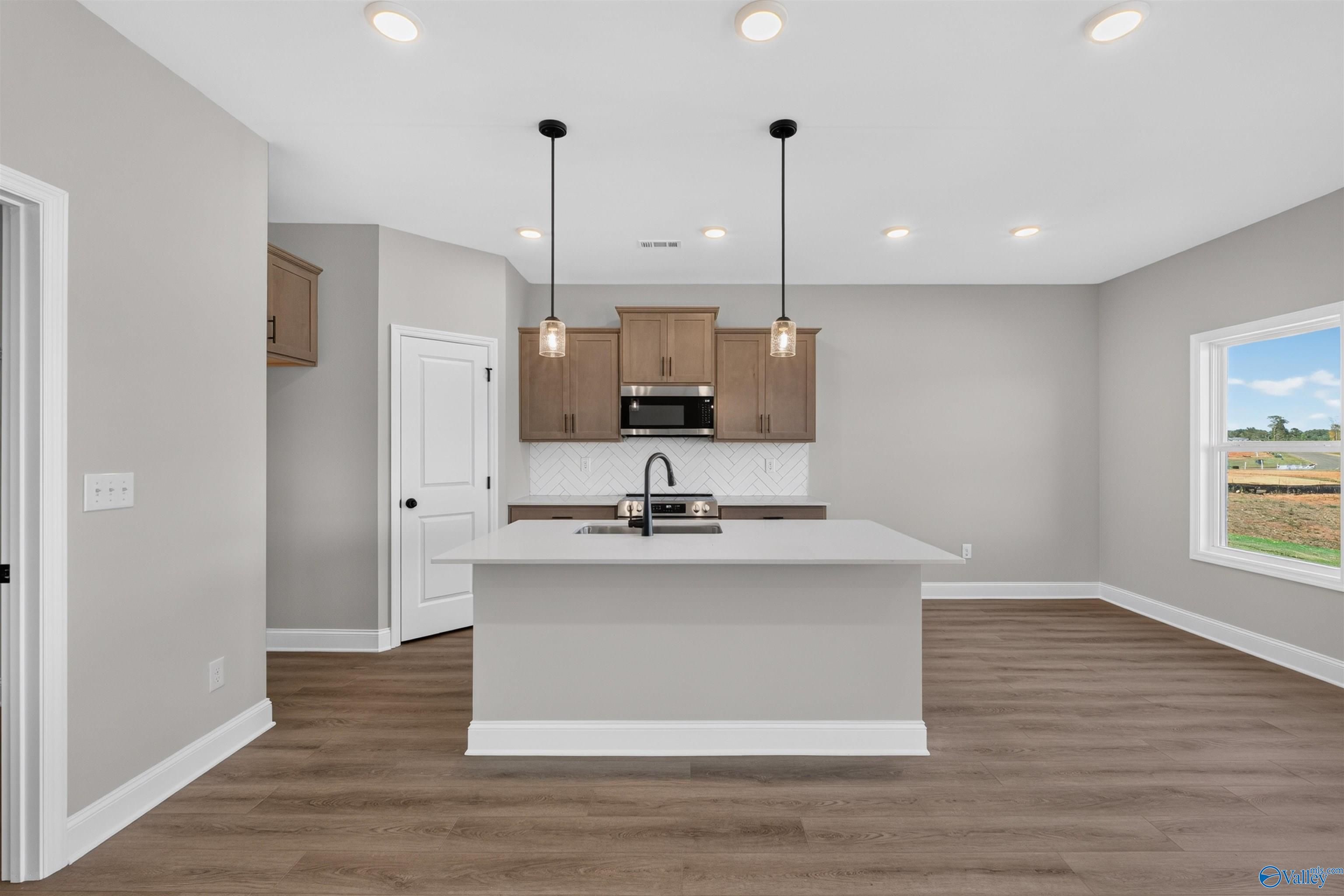 Open-concept kitchen with large island, herringbone backsplash, and wood-look flooring in Davidson Homes Butler plan, Heritage Lakes AL