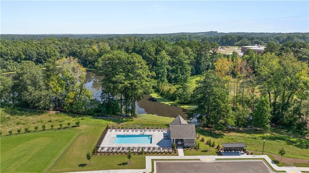 Aerial view of community pool and clubhouse beside scenic lake and lush greenery at Lake Shore by Davidson Homes in Winder, Georgia