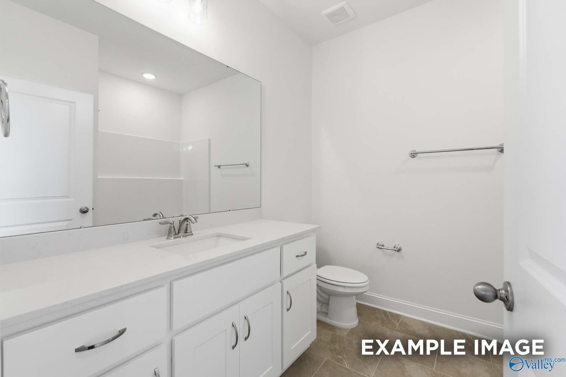 Modern bathroom with white vanity, large mirror, and neutral tile flooring in The Valencia floor plan, Meridianville, AL.
