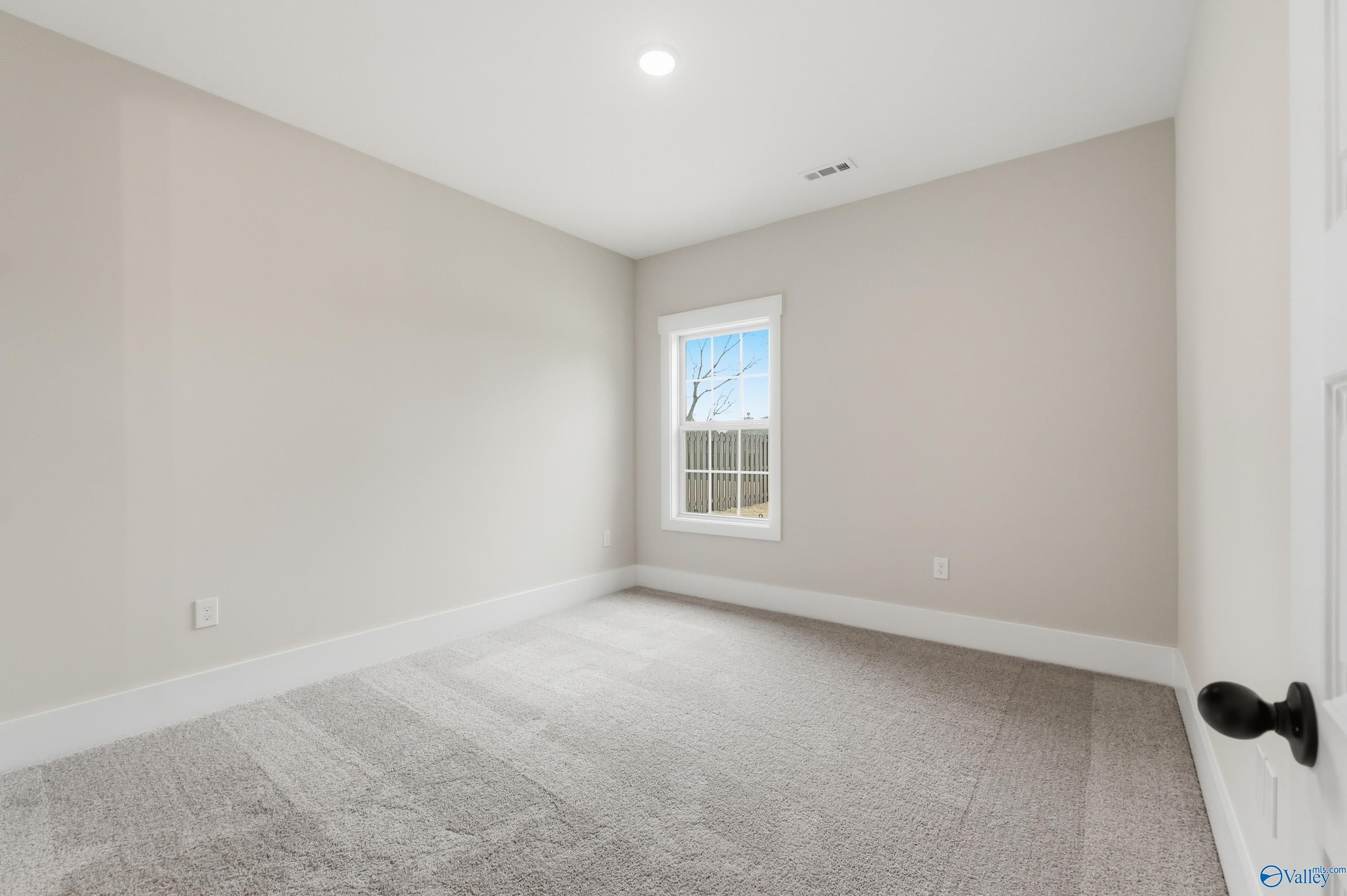 Empty secondary bedroom with neutral beige walls, carpet floor, and window in The Finleigh by Davidson Homes, Meridianville, Alabama