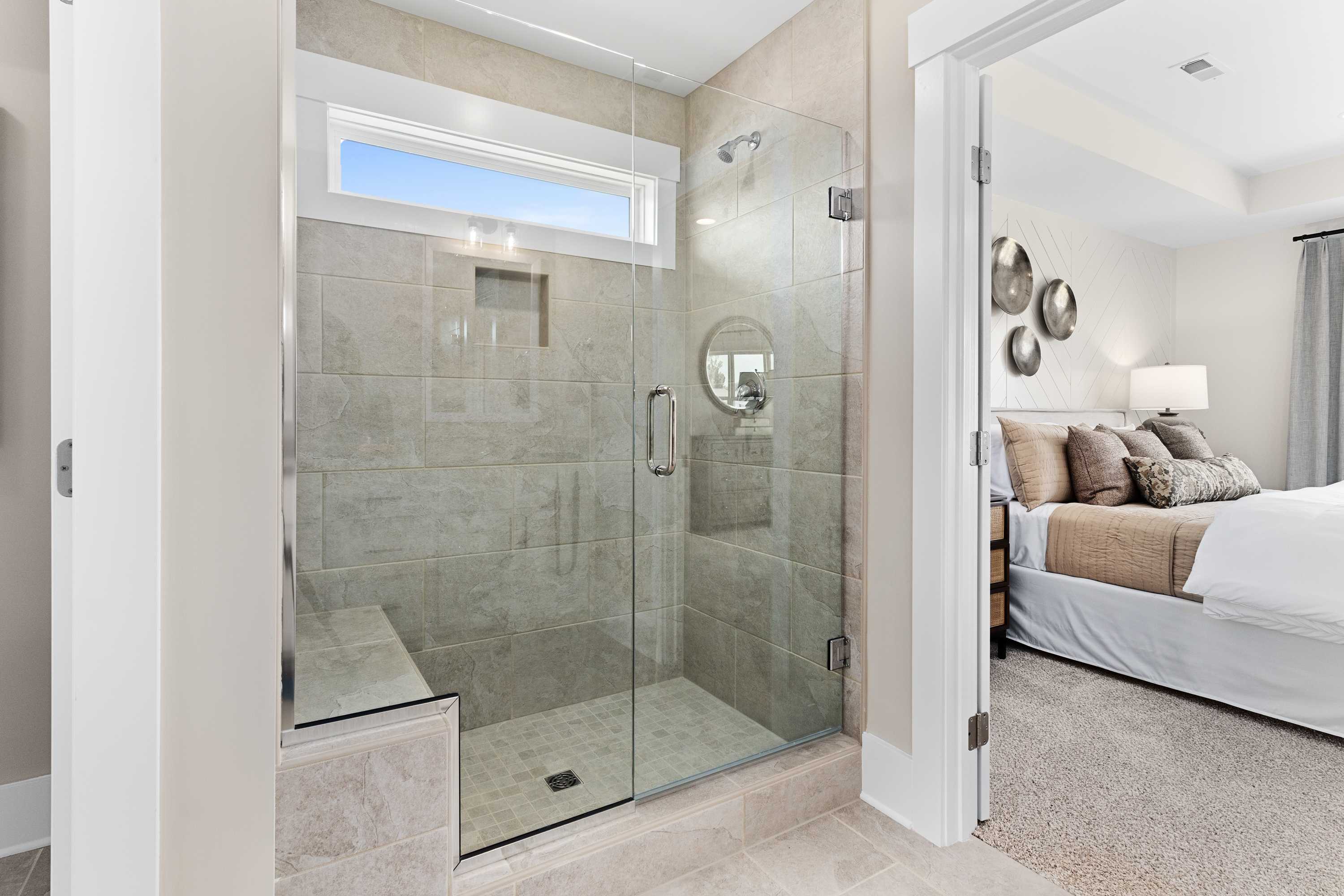 Spacious master bathroom in The Shelby A with frameless glass walk-in shower, built-in bench, and adjacent bedroom