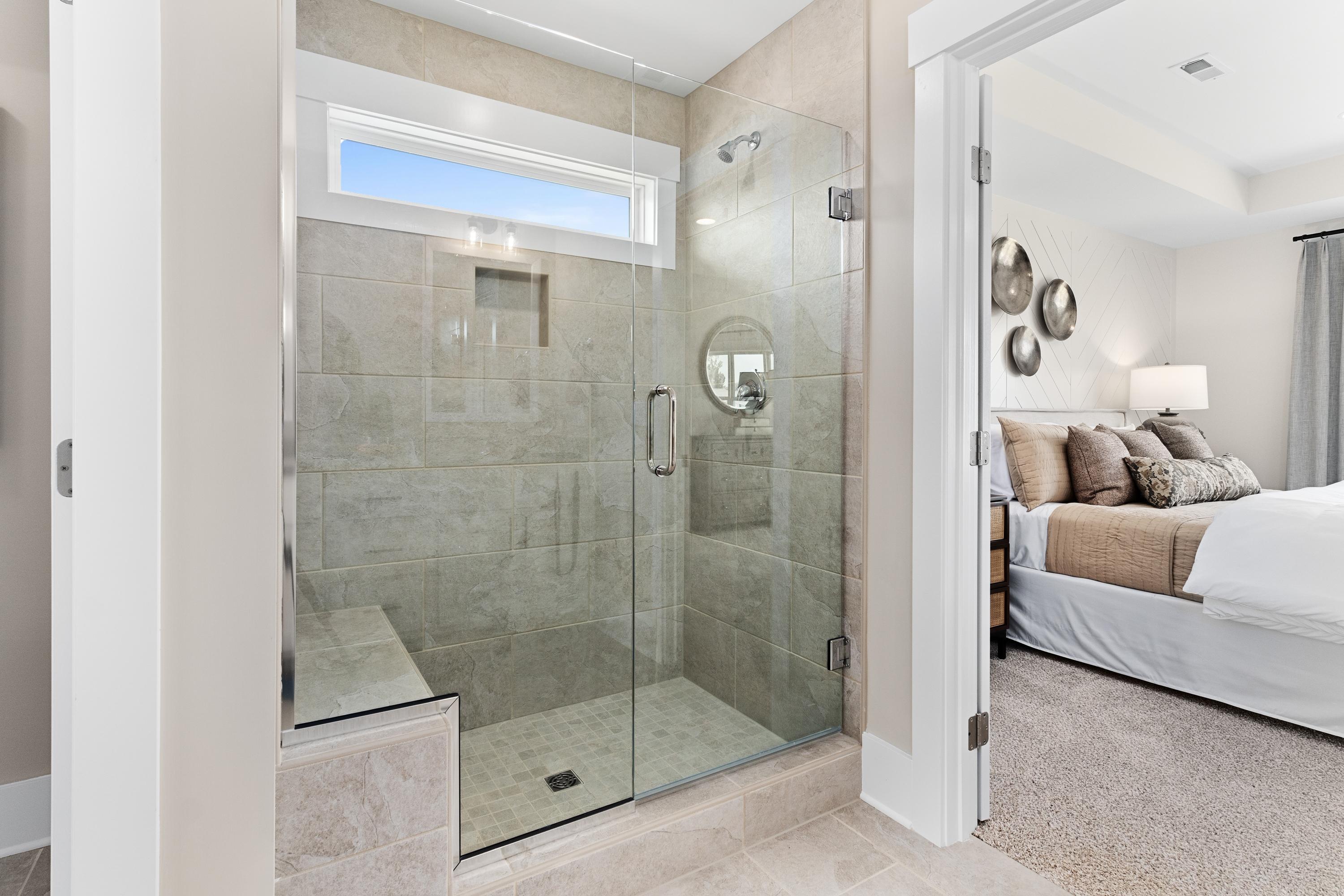 Spacious master bathroom in The Shelby A with frameless glass walk-in shower, built-in bench, and adjacent bedroom