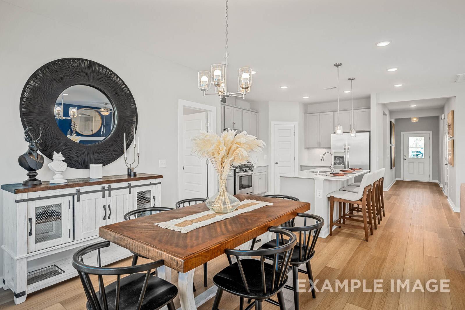 Open-concept dining and kitchen in The Franklin B with farmhouse table, bar stools, sleek cabinets, and large mirror