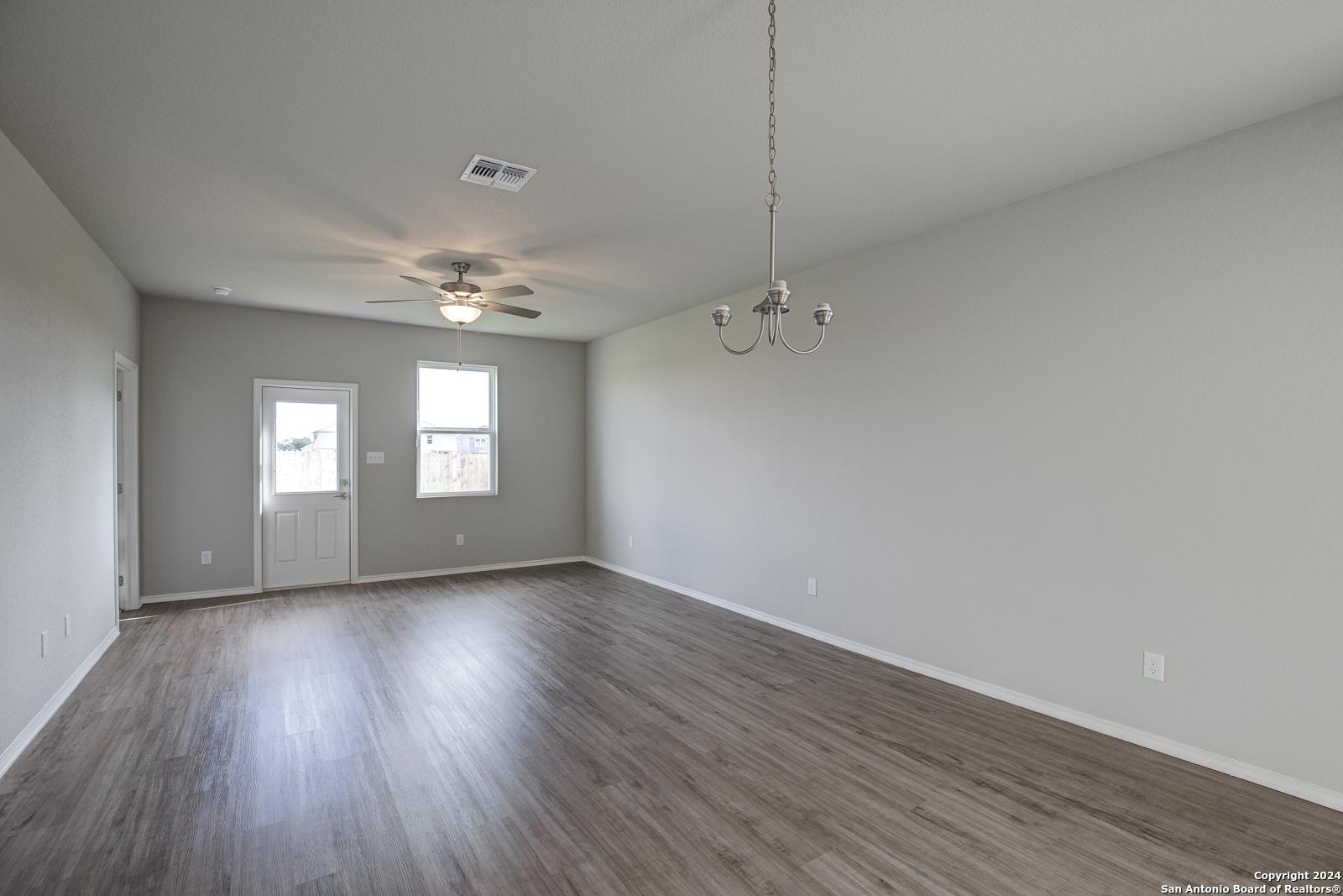 Spacious living room with hardwood floors, ceiling fan, chandelier, and large windows in 3-bedroom Davidson Homes The Frio B, San Antonio
