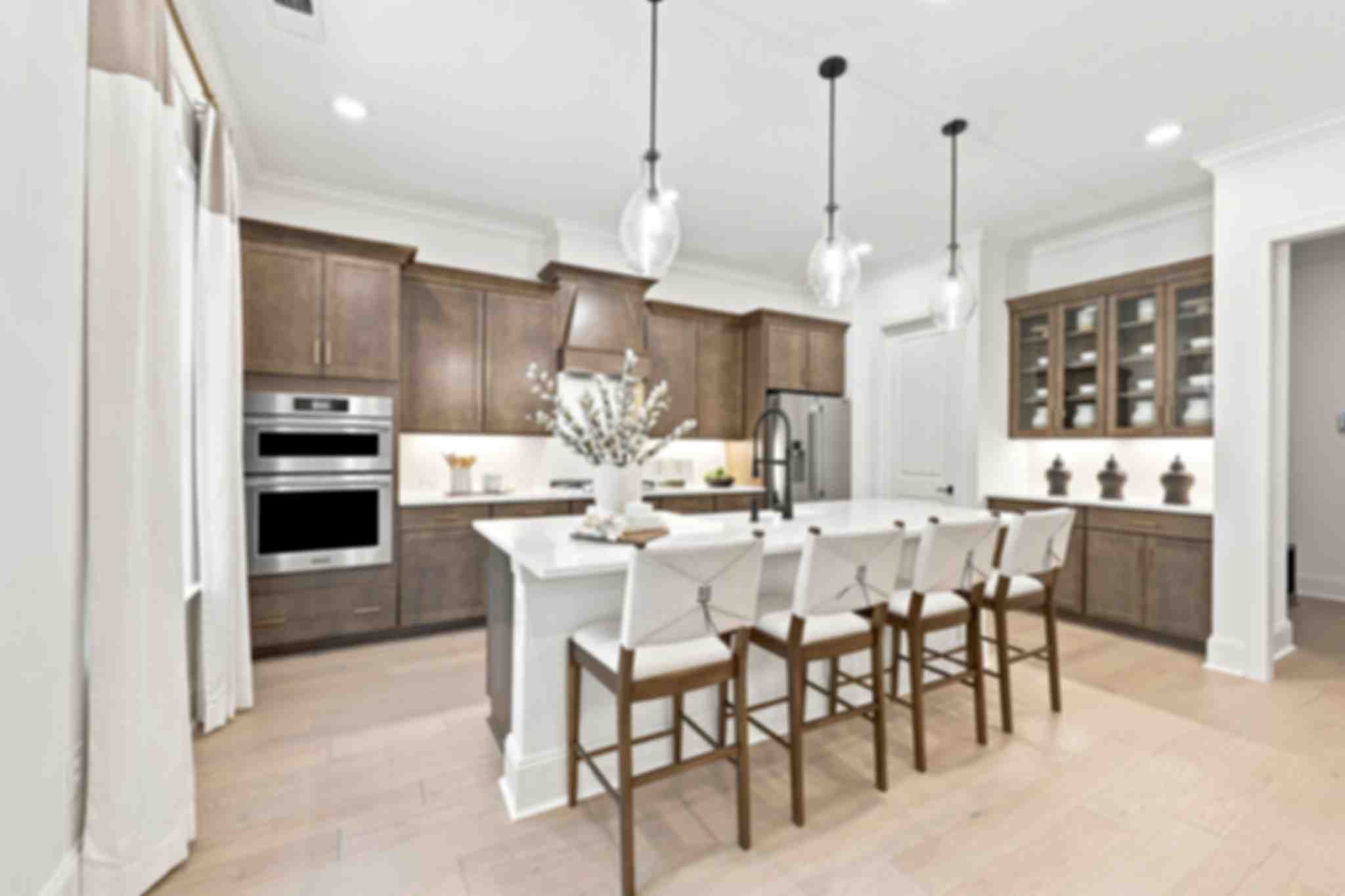 Spacious kitchen at Rockport in Wake Forest NC by Davidson Homes featuring white cabinets, quartz island with leather stools, and pendant lights