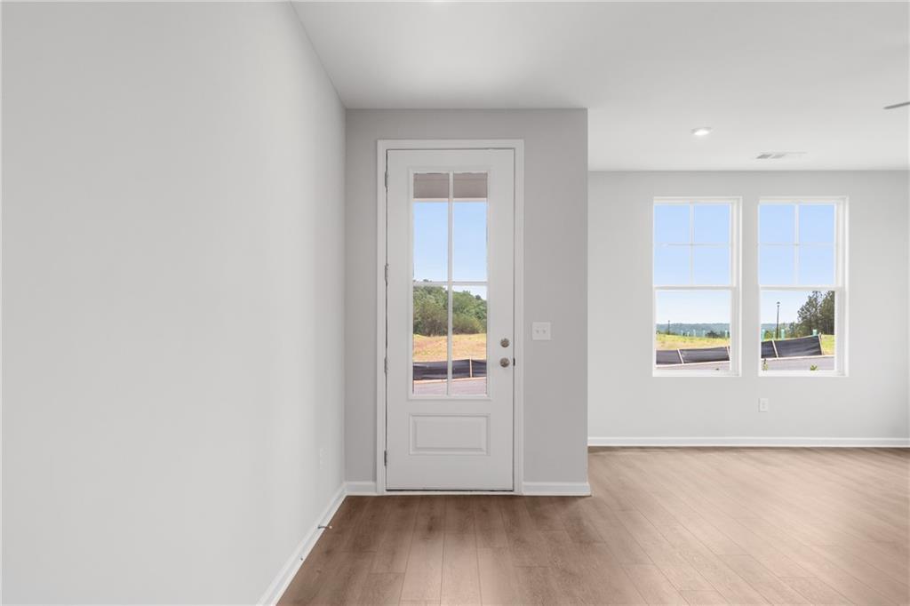 Bright entryway with white glass door, large windows, and wooded view on hardwood floors in The Monroe B home, Emerson, Georgia