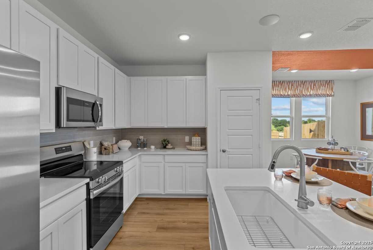 Modern white kitchen with stainless steel appliances, large island sink, and open dining in Davidson Homes The Daphne I, Bricewood, San Antonio