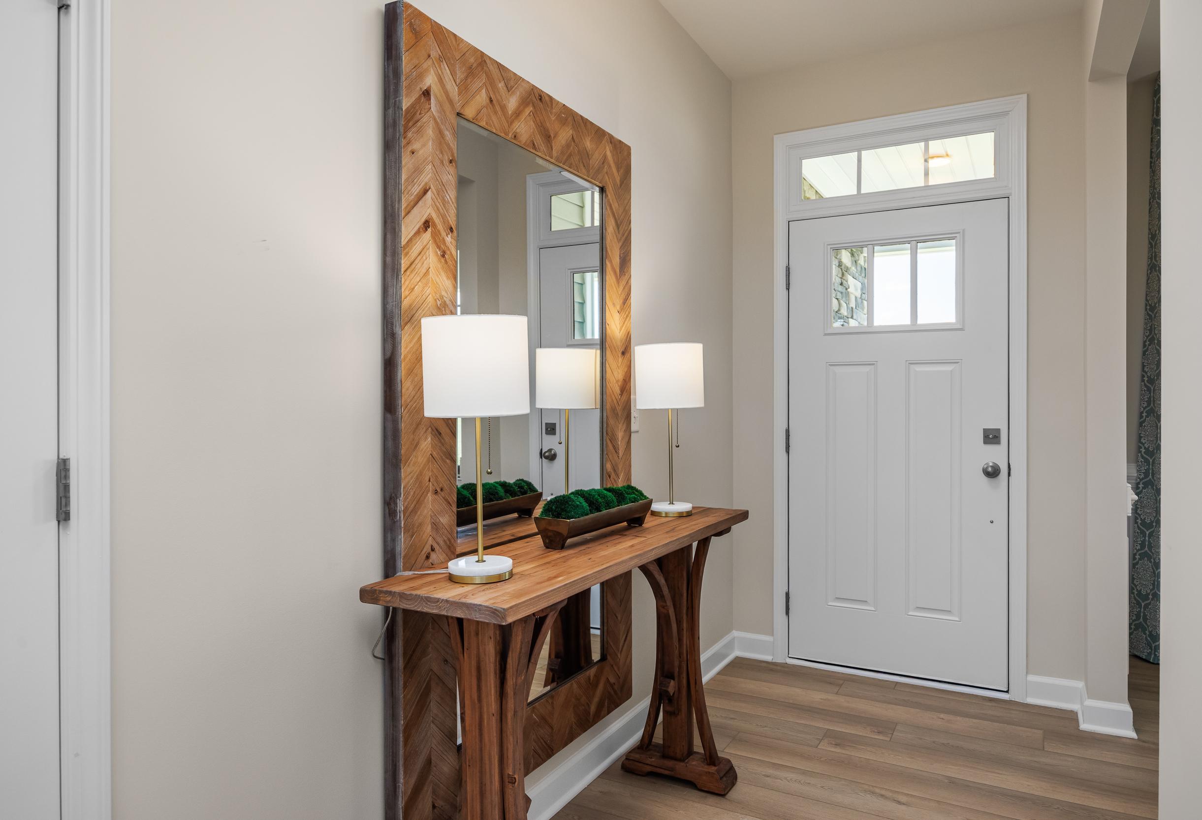 Welcoming foyer in The Willow B model home, featuring a rustic wooden console table, chevron-pattern mirror, and entry door.