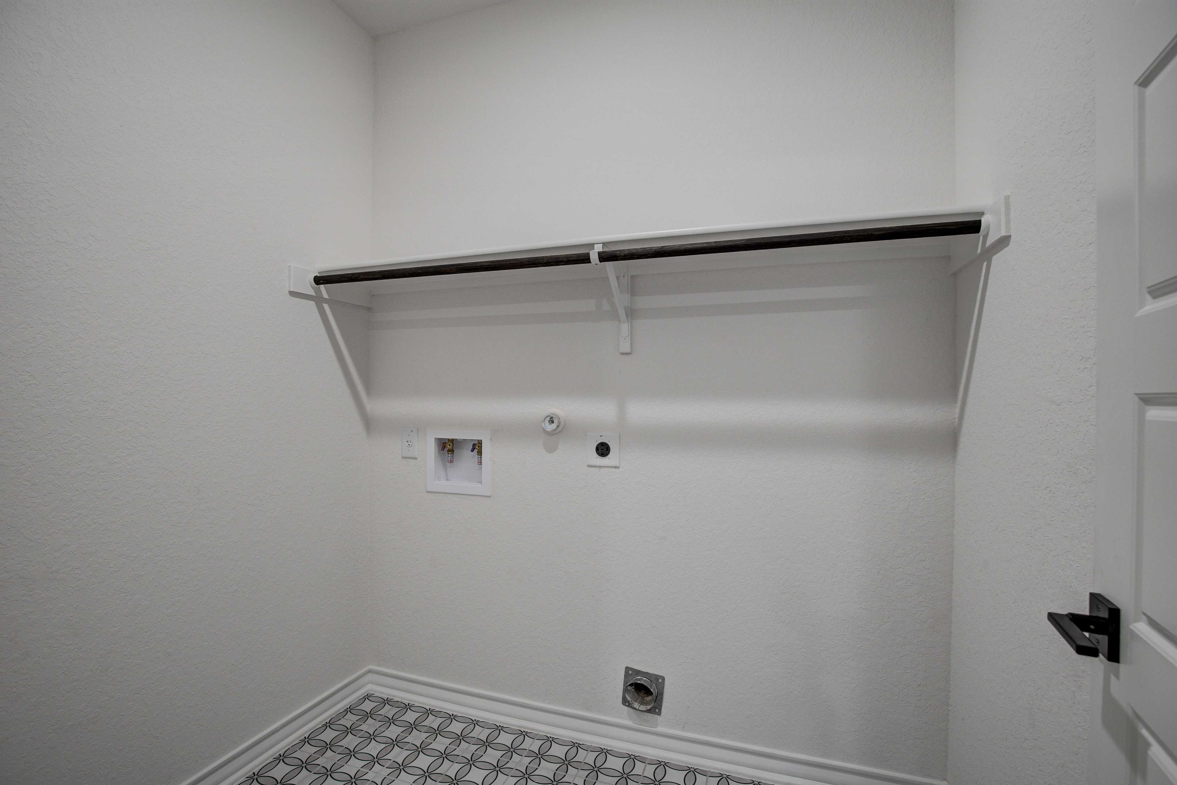 Spacious laundry room in The Lanier Davidson Homes design with built-in shelf, hanging rod, washer-dryer hookups, and checkered tile floor