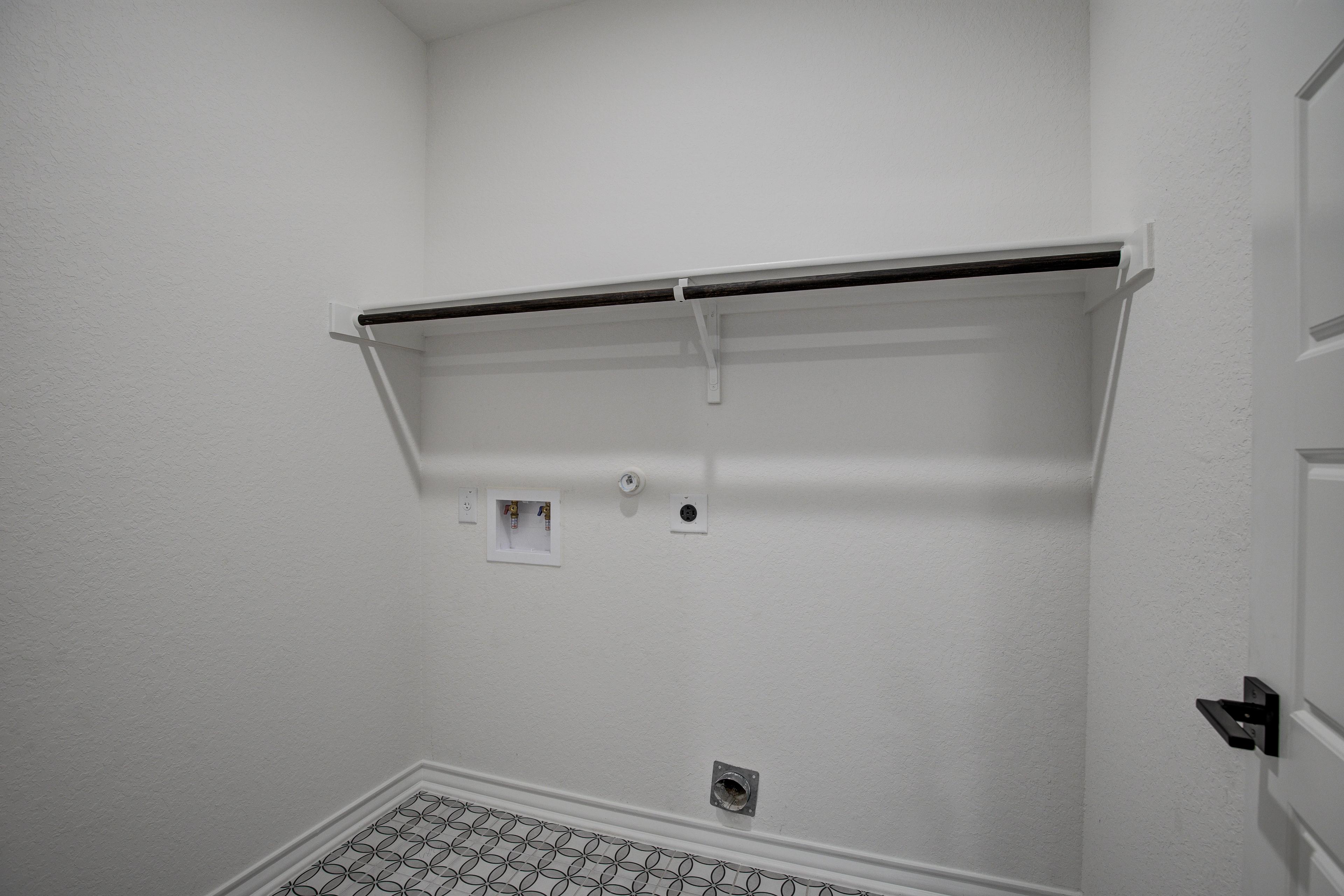 Spacious laundry room in The Lanier floor plan with built-in clothing rod, washer dryer hookups, white walls, and checkered tile floor