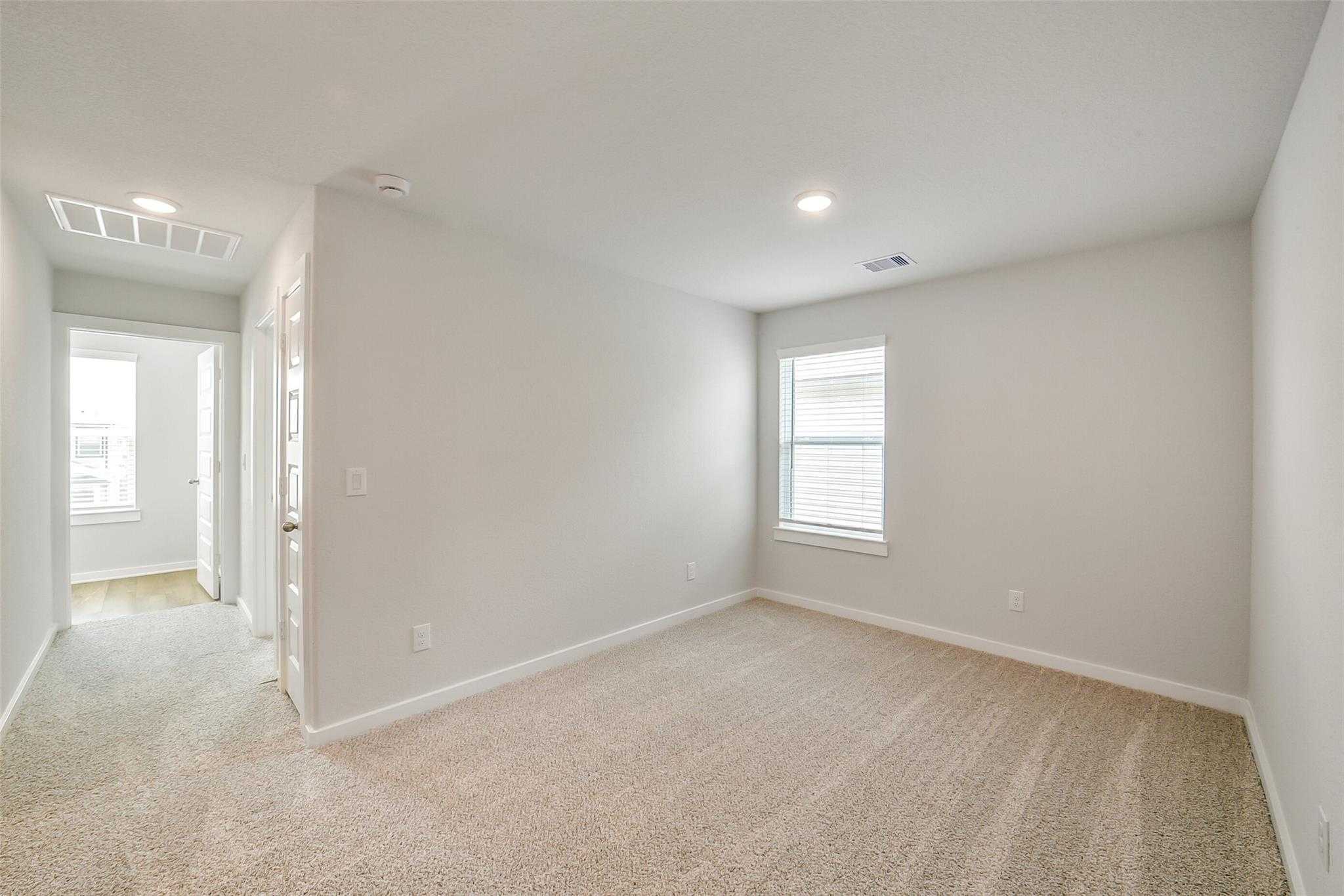 Spacious secondary bedroom with beige carpet, large windows, and adjacent hallway in Davidson Homes The Trinity F, Magnolia, Texas