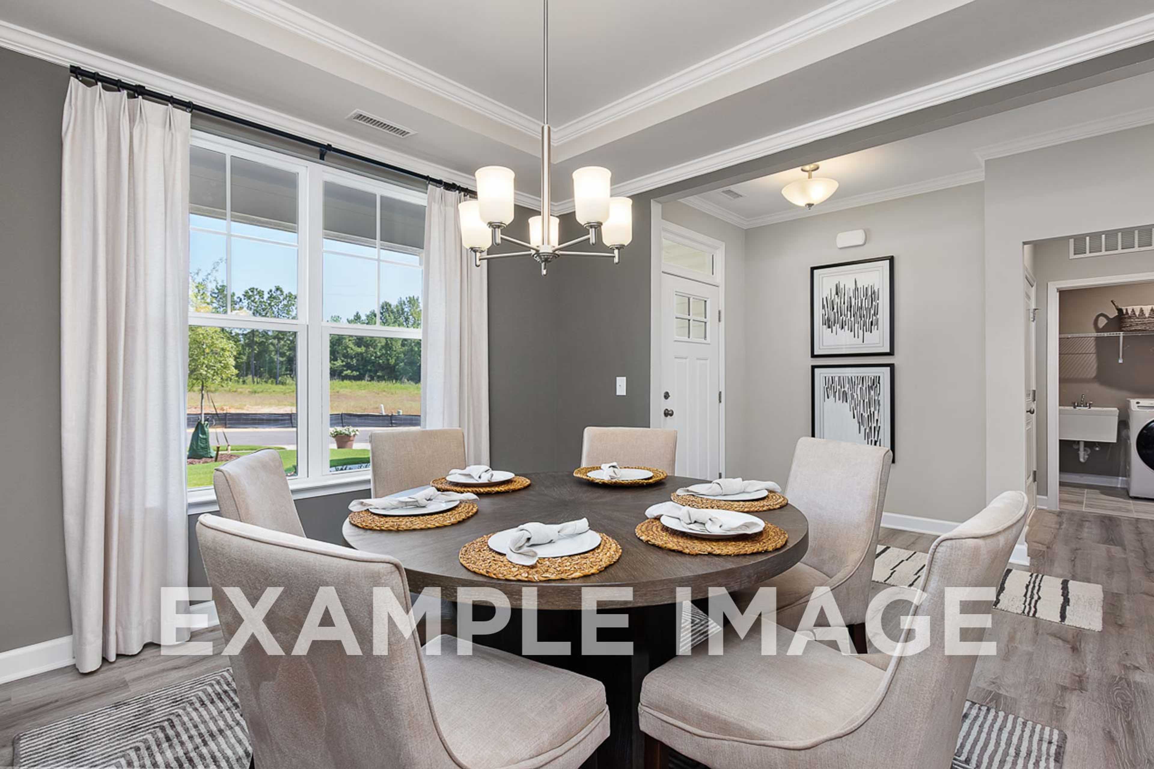 Spacious dining room in The Ash D with round wood table set for six, cream upholstered chairs, chandelier, large windows to greenery