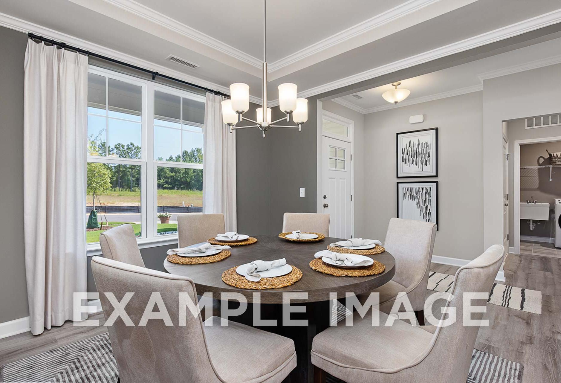 Spacious dining room in The Ash D with round wood table set for six, cream upholstered chairs, chandelier, large windows to greenery