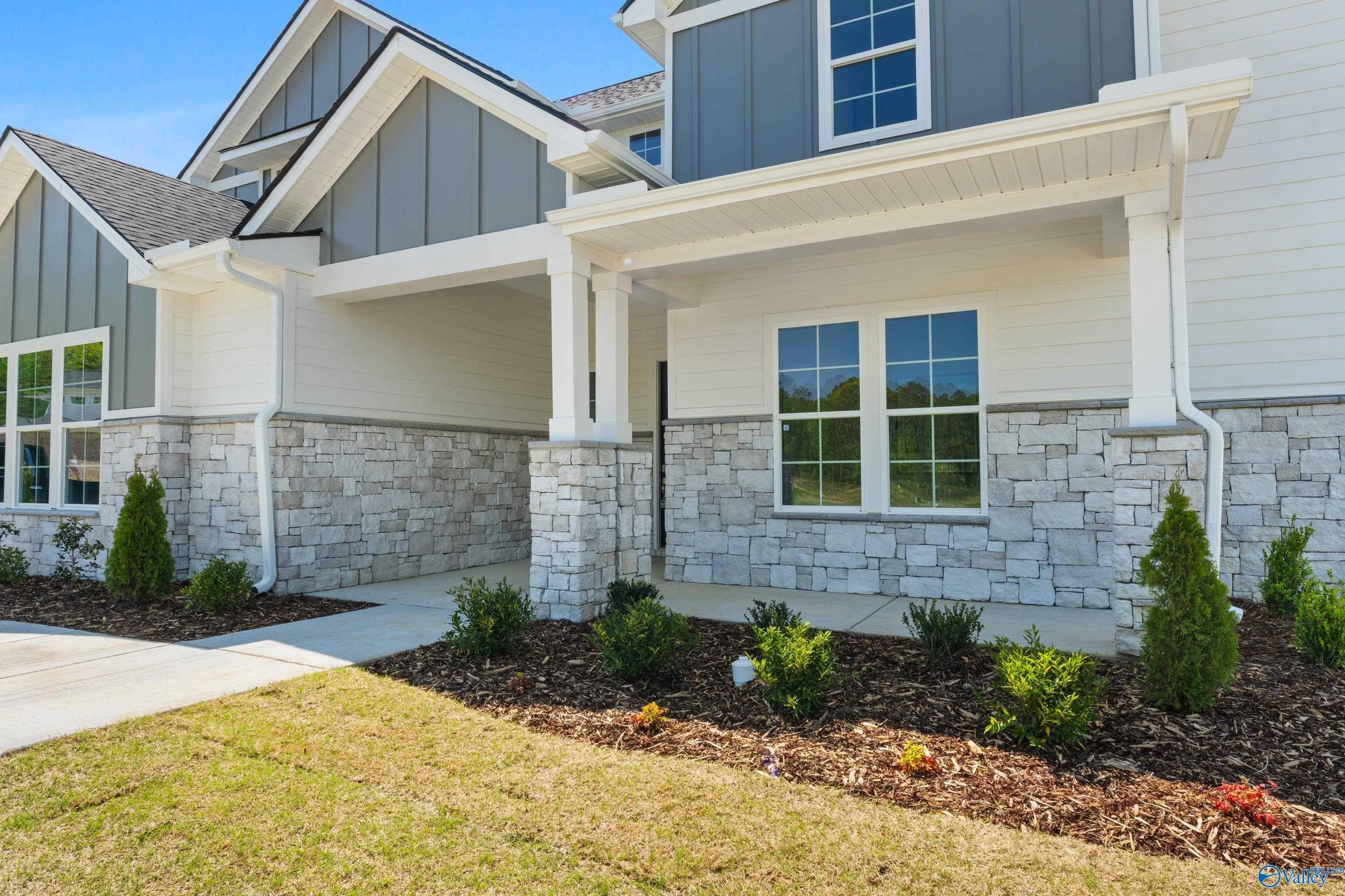 Modern two-story home exterior with stone accents, covered porch, large windows, and landscaped yard in The Meadows at Hampton Cove, Owens Cross Roads, Alabama