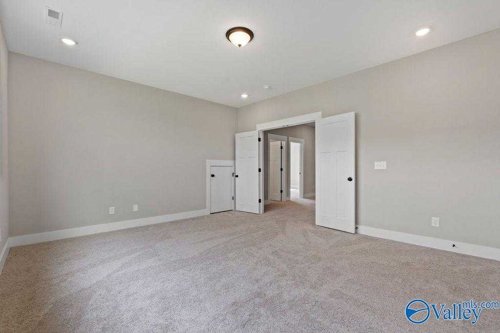 Spacious empty bedroom with beige walls, carpeted floor, ceiling fan, and open double doors in Evermore Homes Oxford plan, Owens Cross Roads, AL