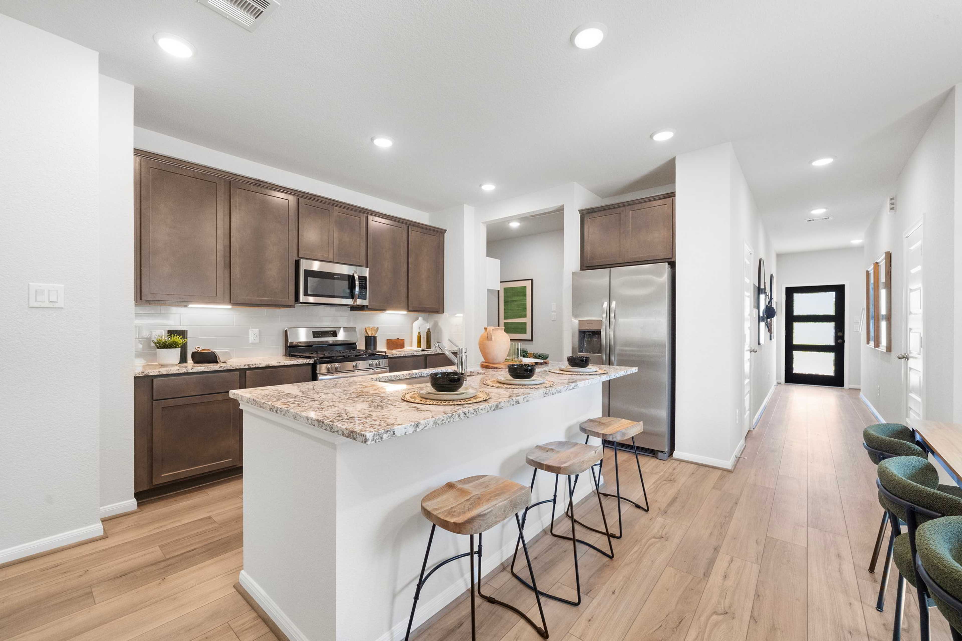 Modern kitchen with brown cabinets, granite island, bar stools, and stainless appliances at Caney Creek Place in Conroe TX