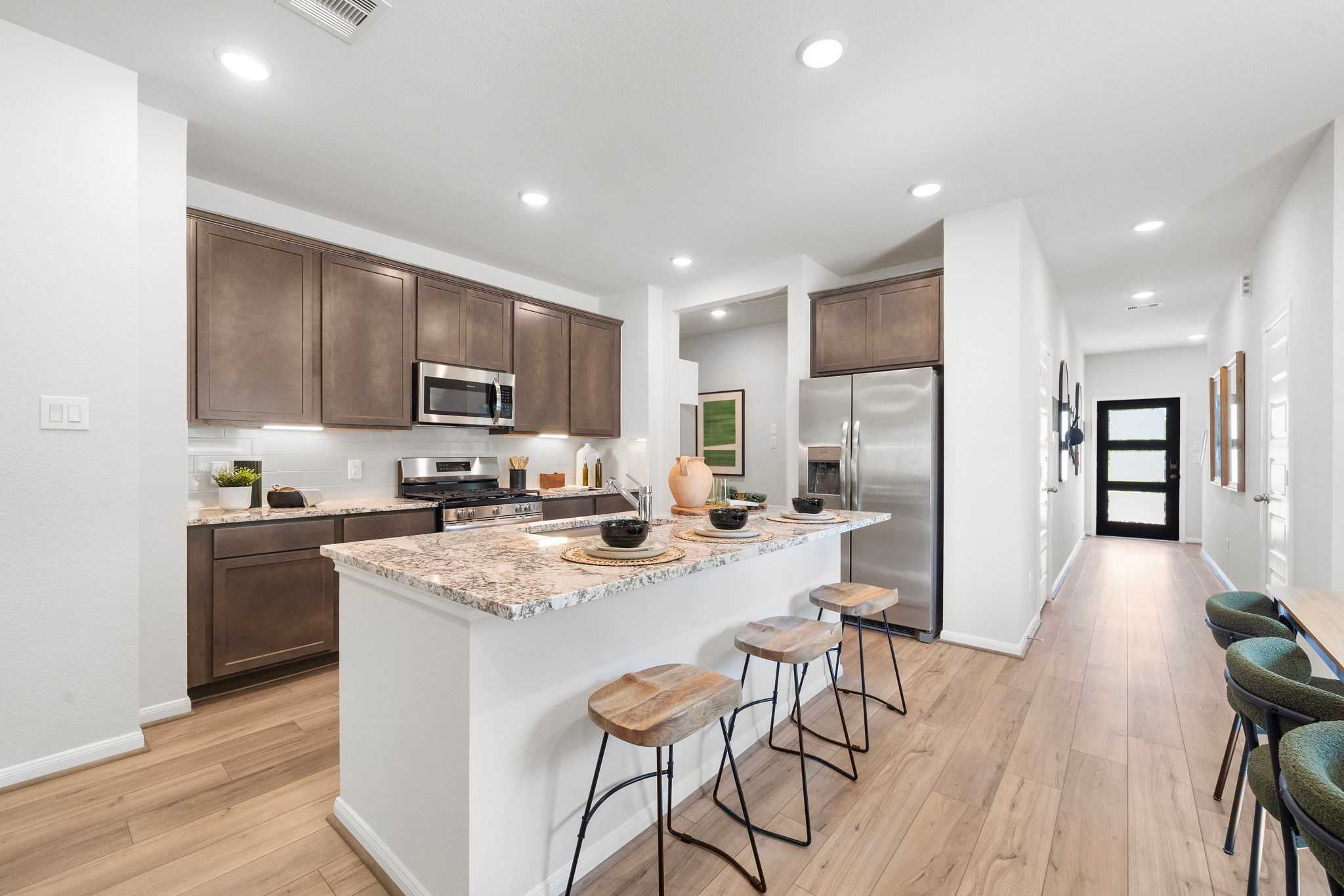 Modern kitchen with brown cabinets, granite island, bar stools, and stainless appliances at Caney Creek Place in Conroe TX