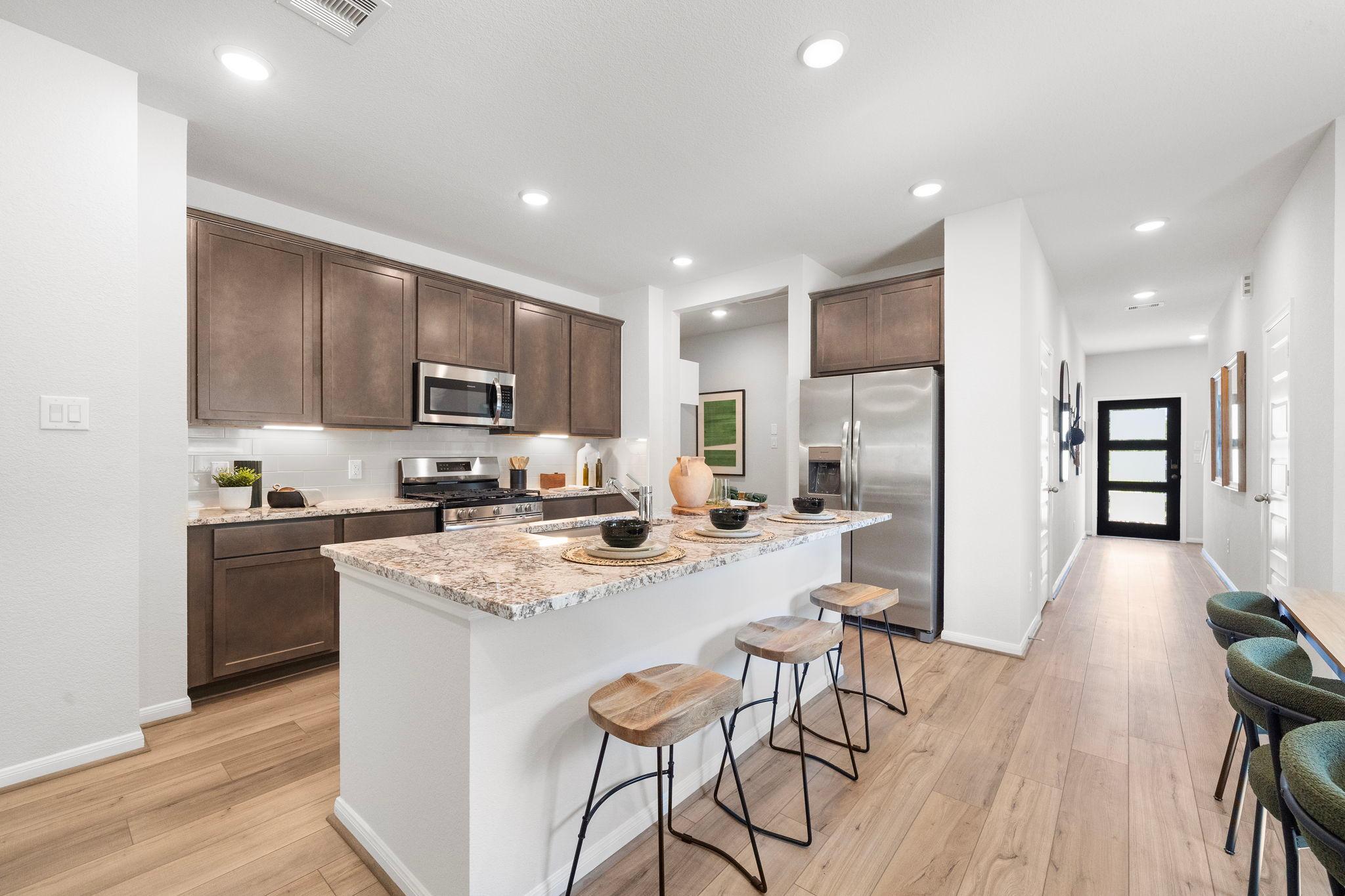 Modern kitchen with brown cabinets, granite island, bar stools, and stainless appliances at Caney Creek Place in Conroe TX