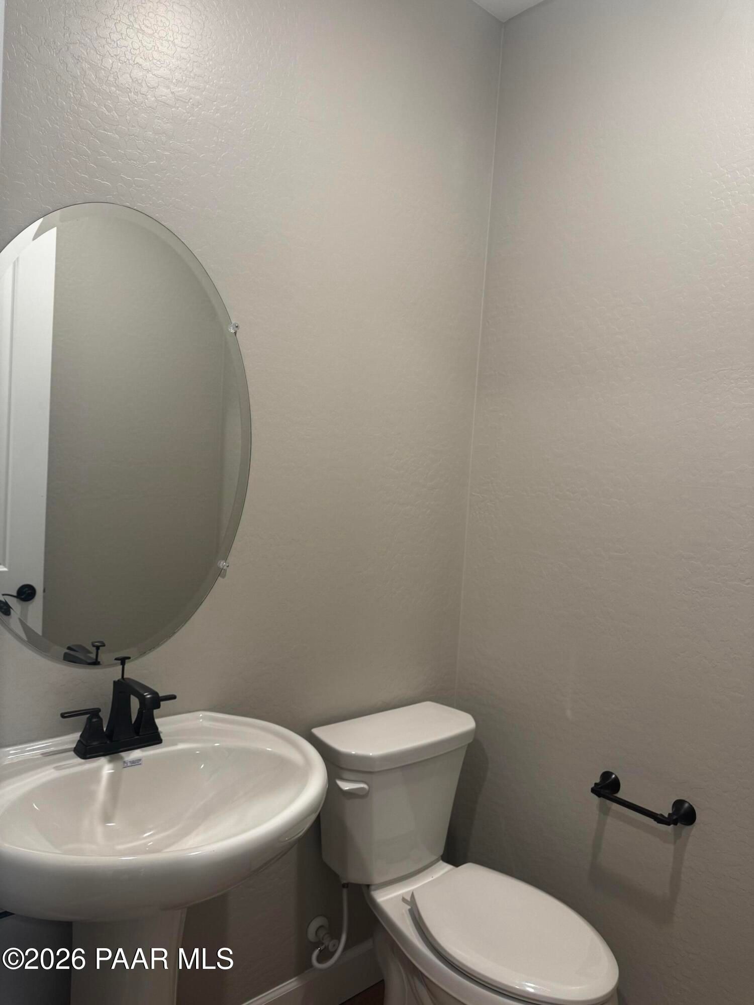 Modern powder room with round mirror, white pedestal sink, black faucet, and toilet in light gray walls, The Monarch B by Evermore Homes, Prescott Valley AZ