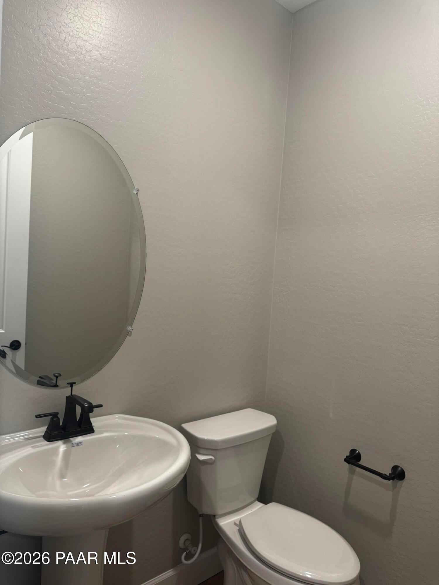Modern powder room with round mirror, white pedestal sink, black faucet, and toilet in light gray walls, The Monarch B by Evermore Homes, Prescott Valley AZ