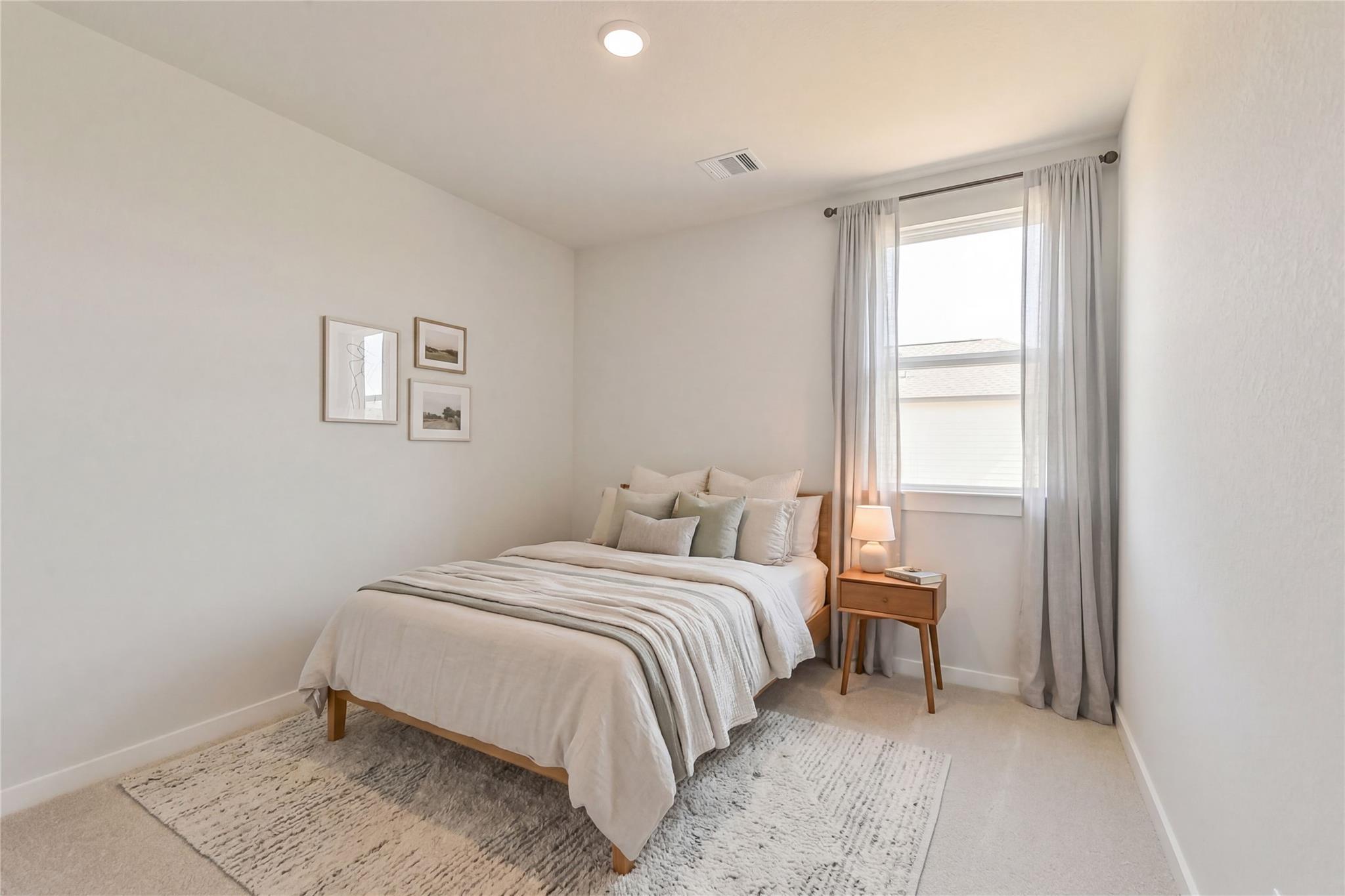 Cozy bedroom with wooden bed, neutral bedding, sheer curtains, wall art and bedside lamp in Davidson Homes The Frio G, Conroe Texas