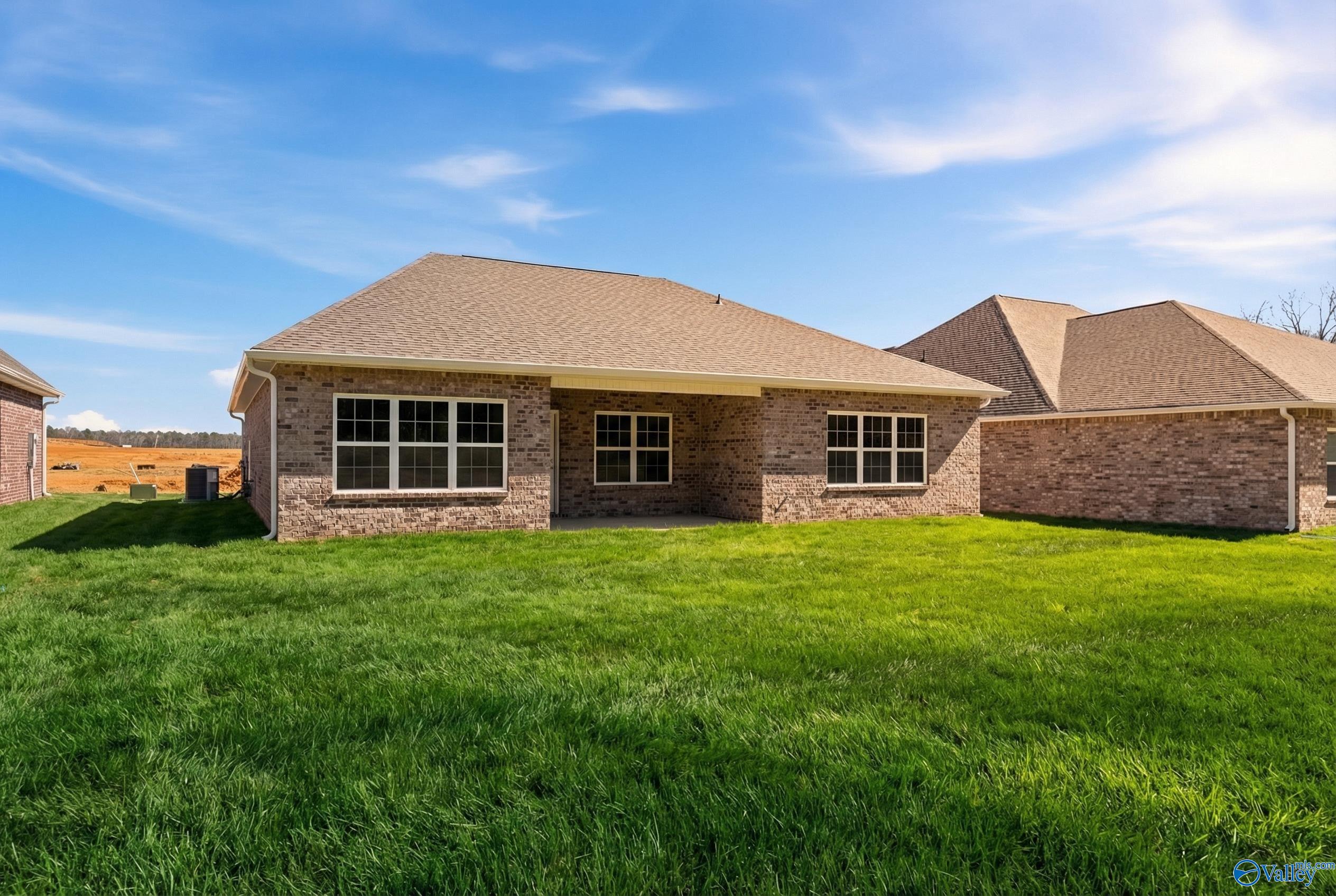 Single-story brick home with covered patio, large windows, and lush green lawn under blue sky in Cain Park, Hartselle, Alabama