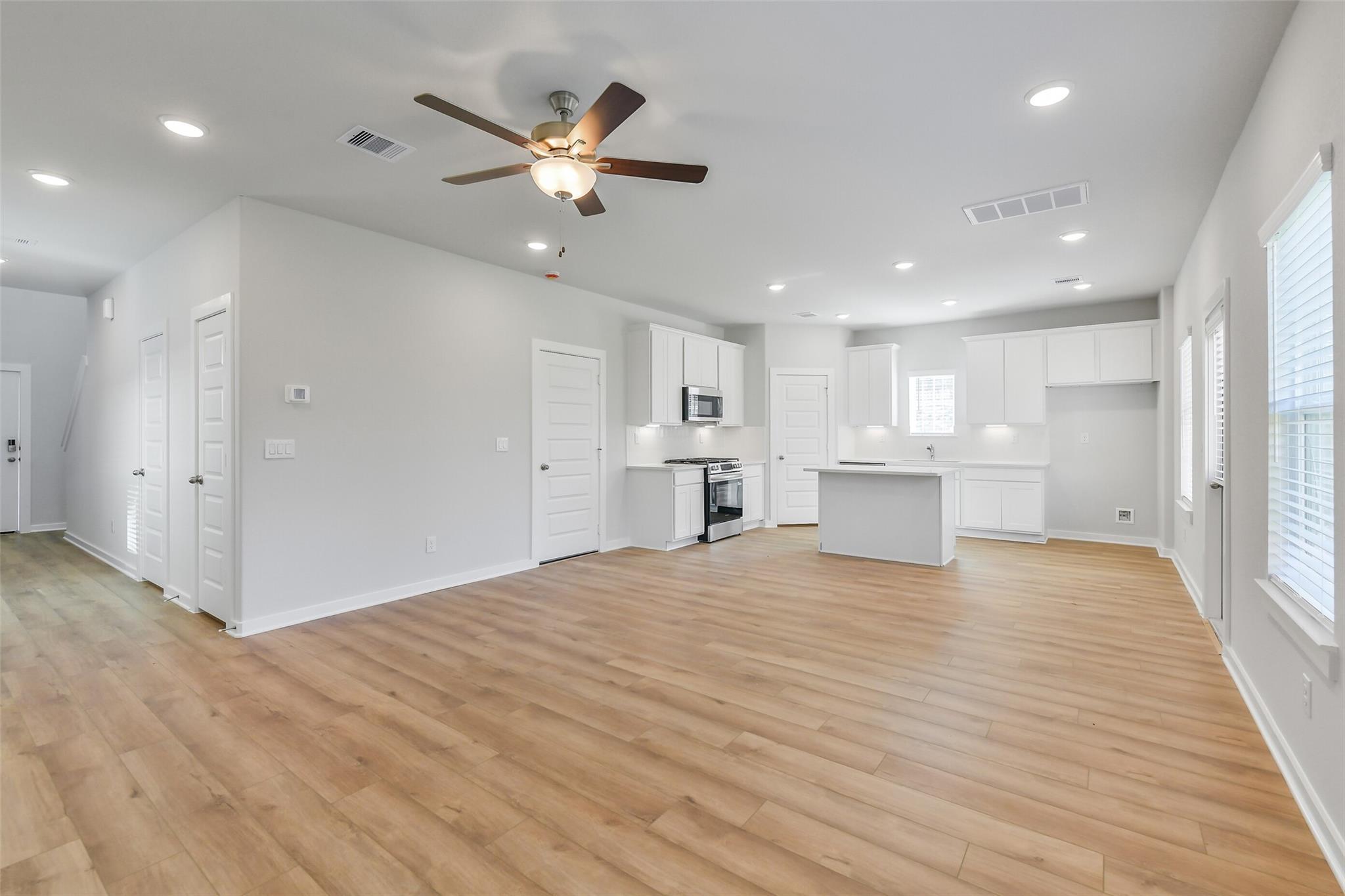 Bright open-concept kitchen-living area with white cabinets, island, ceiling fan, and hardwood floors in Davidson Homes The Trinity F, Magnolia TX