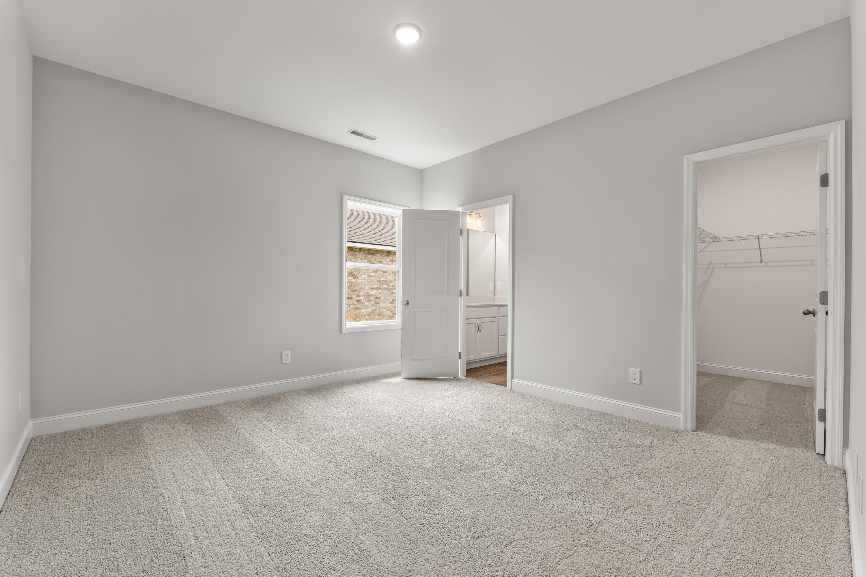 Spacious secondary bedroom in The Butler home design with gray walls, carpet flooring, window blinds, and open walk-in closet