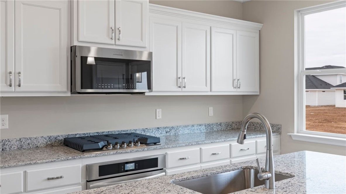 Modern kitchen with white shaker cabinets, granite countertops, gas cooktop, and stainless appliances in Evermore Homes The Stella D, Cusseta, Alabama