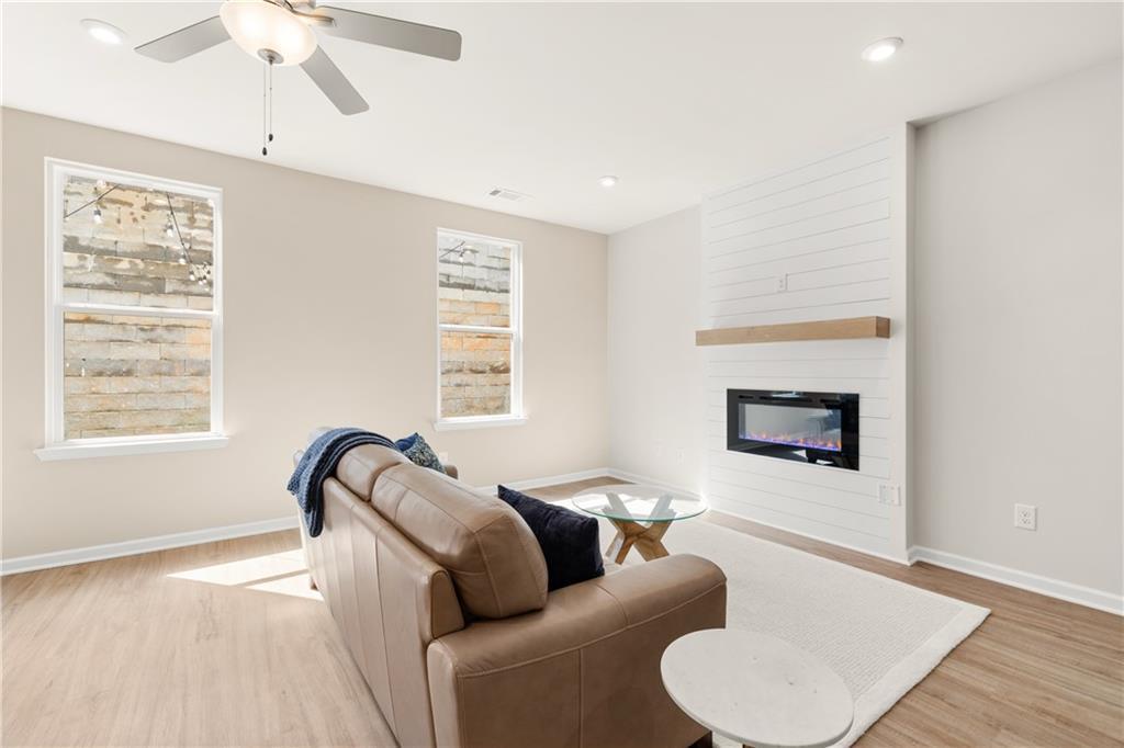 Cozy living room with beige leather sectional, shiplap gas fireplace, ceiling fan, and hardwood floors in Davidson Homes The Marion B, Kennesaw, Georgia
