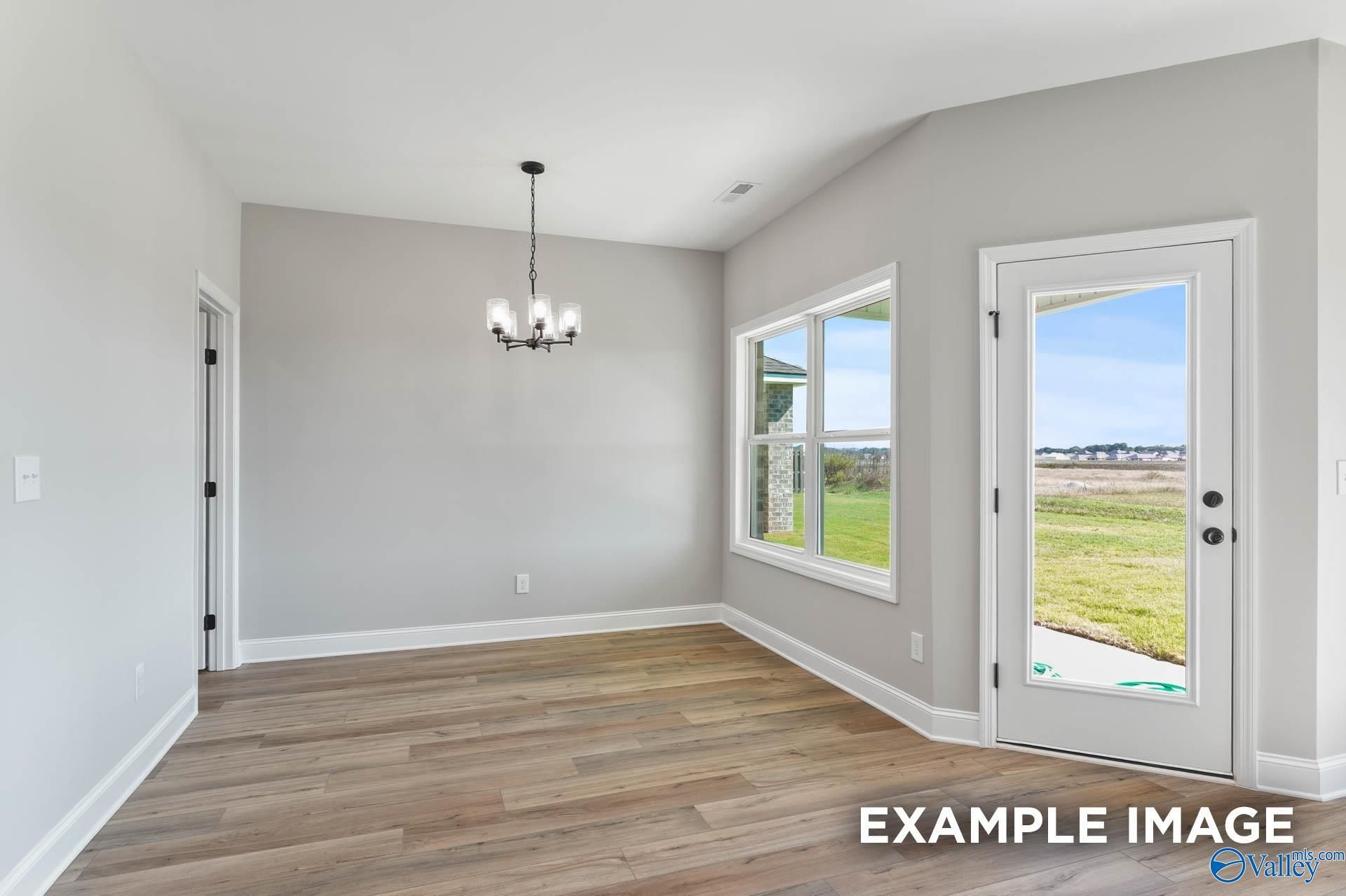 Bright dining room with gray walls, hardwood floors, chandelier, and glass door to green backyard in Davidson Homes The Daphne C, Athens, AL