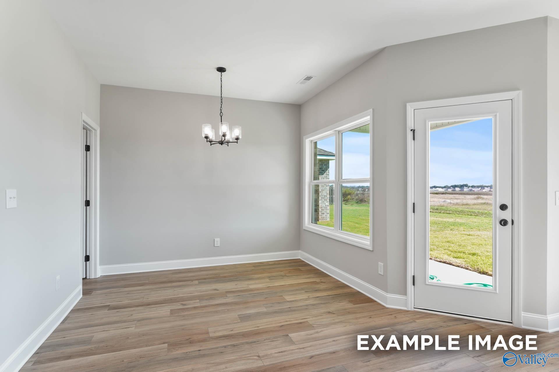 Bright dining room with gray walls, hardwood floors, chandelier, and glass door to green backyard in Davidson Homes The Daphne C, Athens, AL