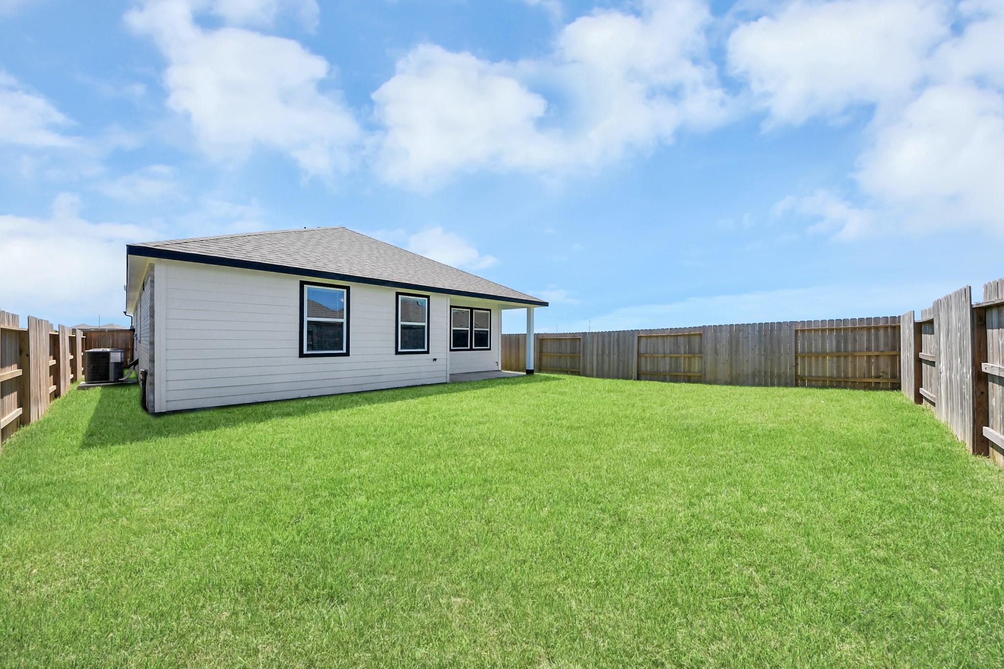 Large fenced backyard with lush green lawn behind white Davidson Homes Costa A in Emberly, Beasley, Texas