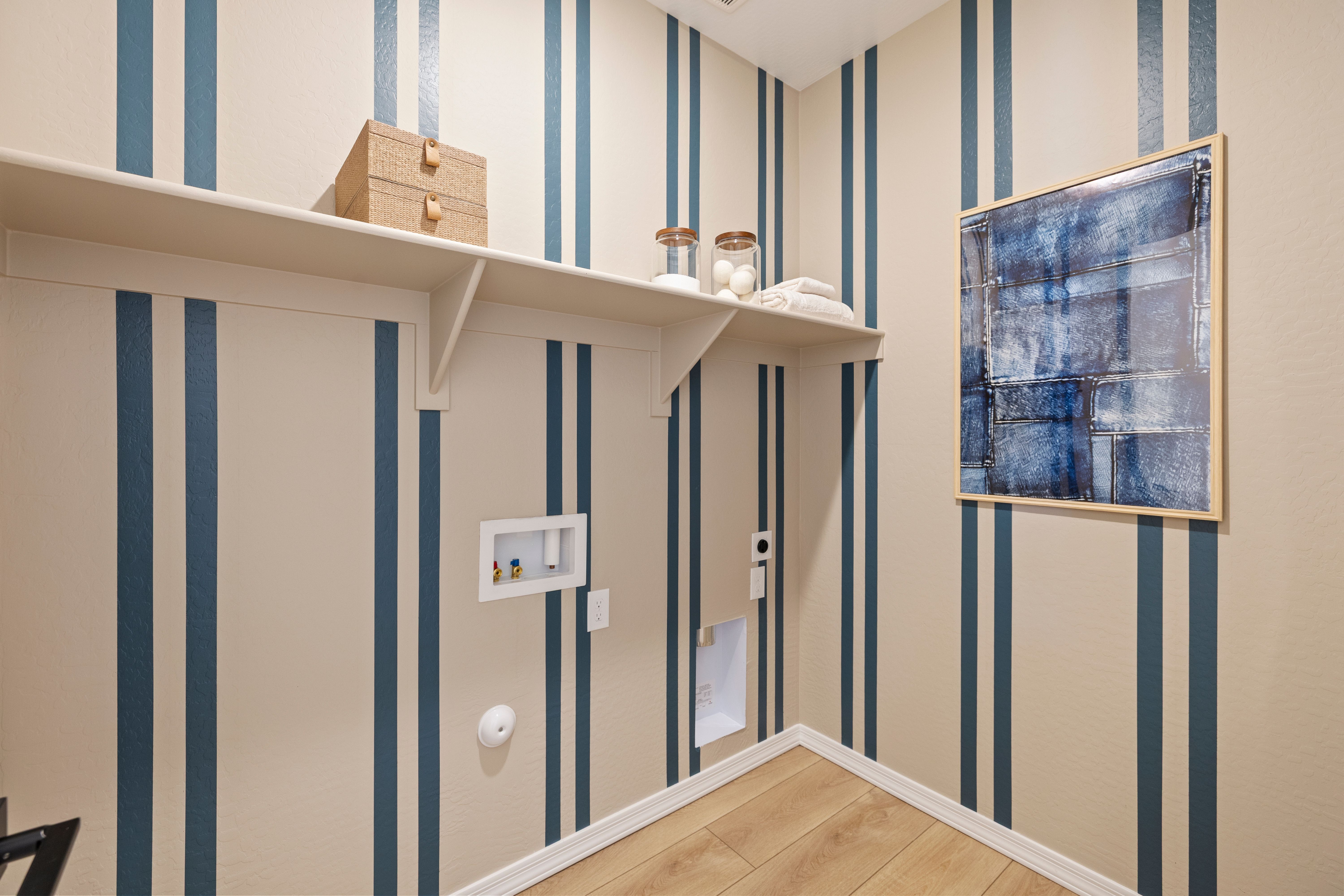 Stylish laundry room at Vineyards at Cottonwood in Cottonwood AZ with navy striped walls, white shelves, storage jars, and abstract blue artwork