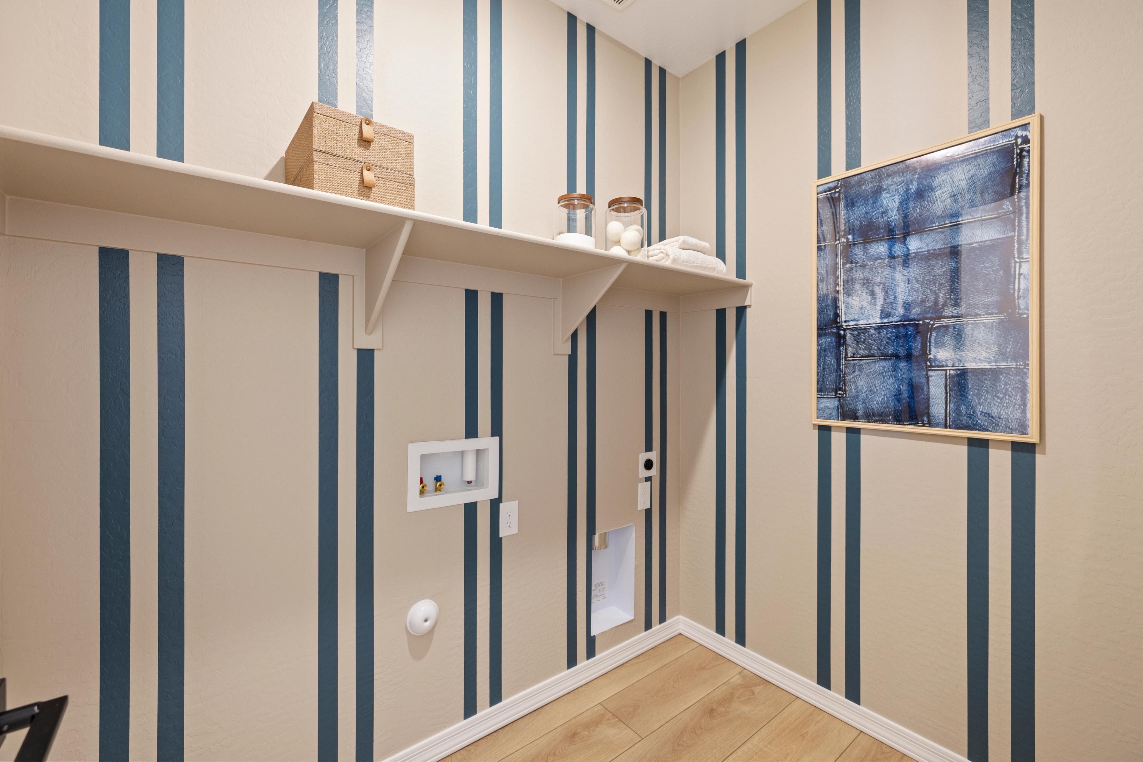 Stylish laundry room at Vineyards at Cottonwood in Cottonwood AZ with navy striped walls, white shelves, storage jars, and abstract blue artwork
