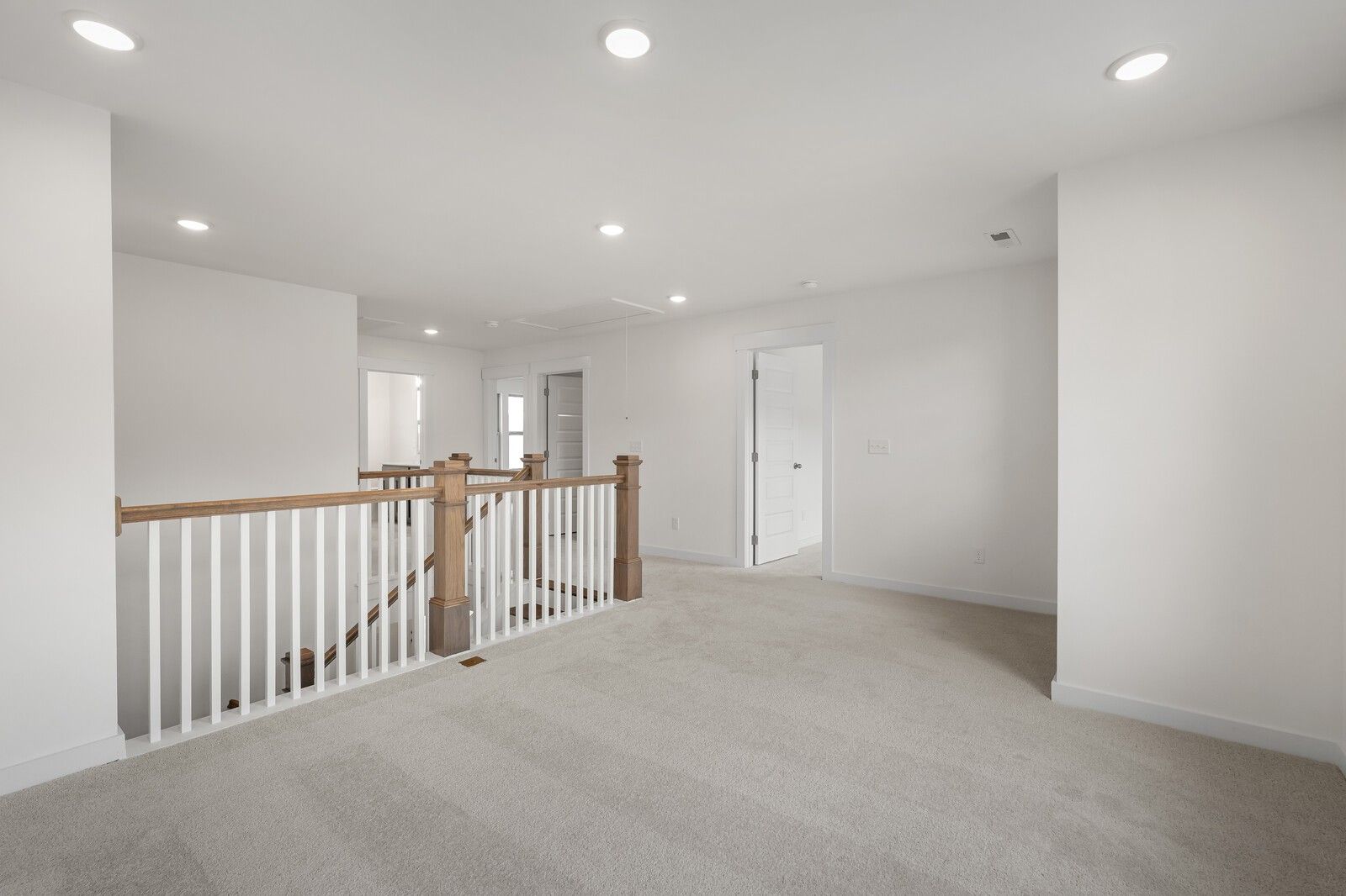 Spacious upstairs hallway with white walls, carpeted floors, and oak balustrade staircase in Davidson Homes The Willow C, Gallatin, Tennessee