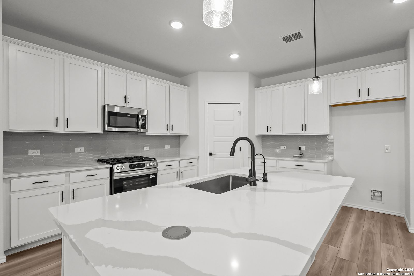Modern white kitchen with quartz island, stainless appliances, subway tile backsplash in Davidson Homes The Douglas E, San Antonio